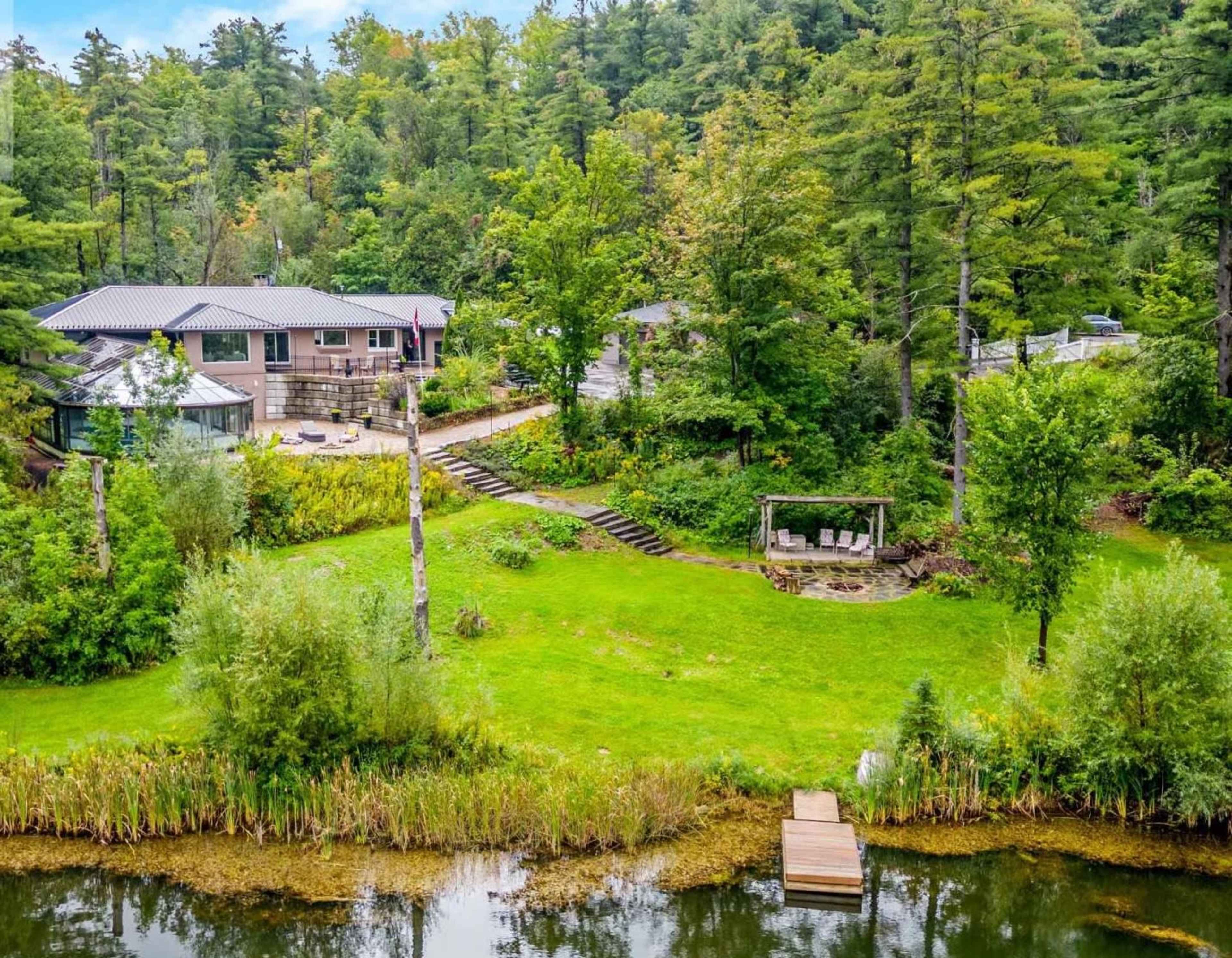 The image shows a lakeside property with a modern house, surrounded by greenery and a dock extending into the water.