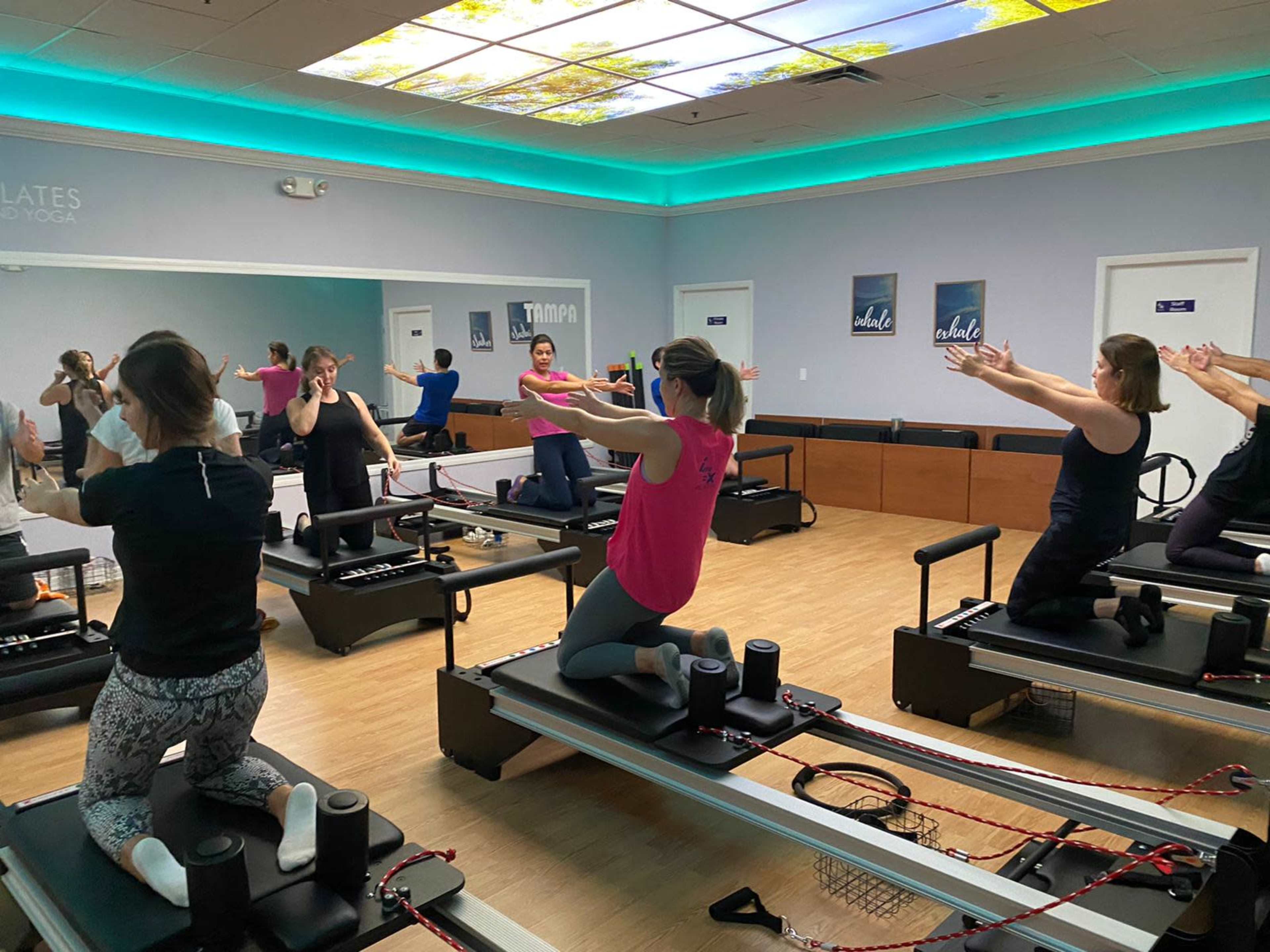A group of individuals is practicing Pilates on reformer machines in a well-lit studio.