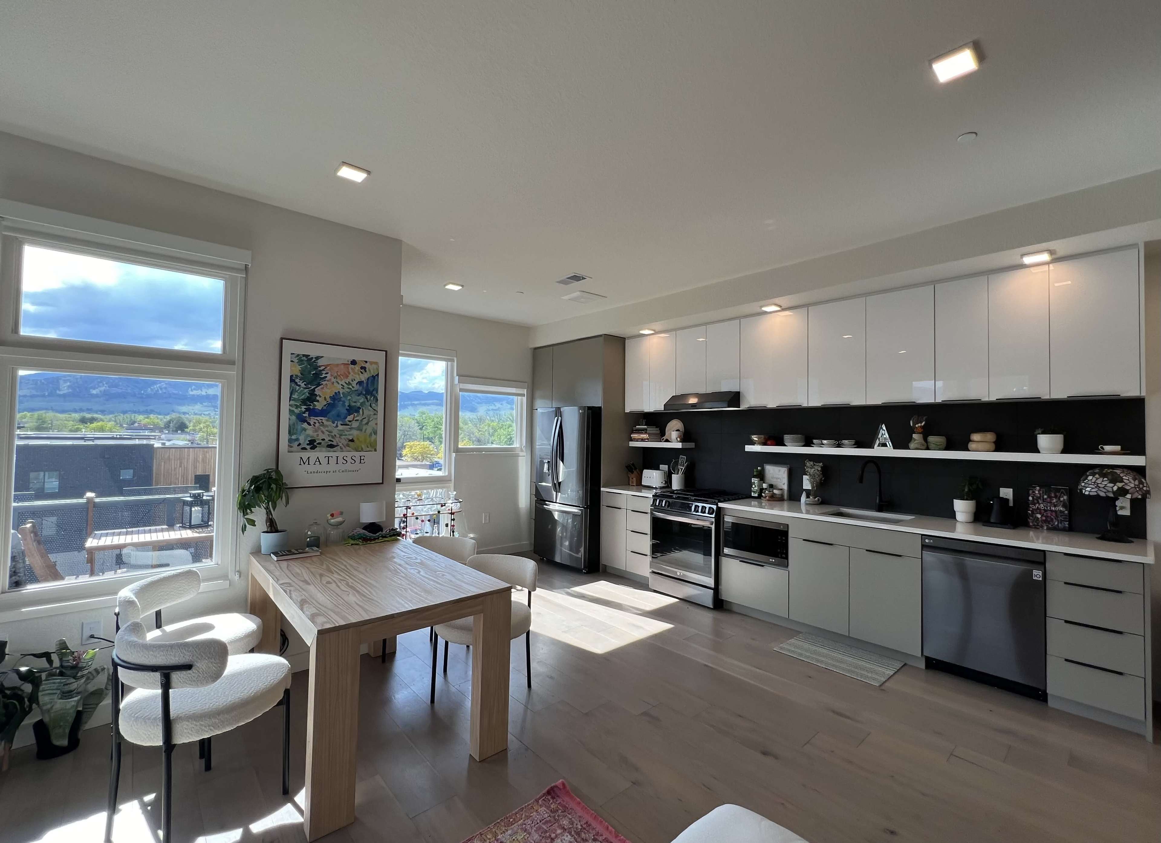A modern kitchen with a dining table, large windows showing a mountainous view, and sleek cabinetry.