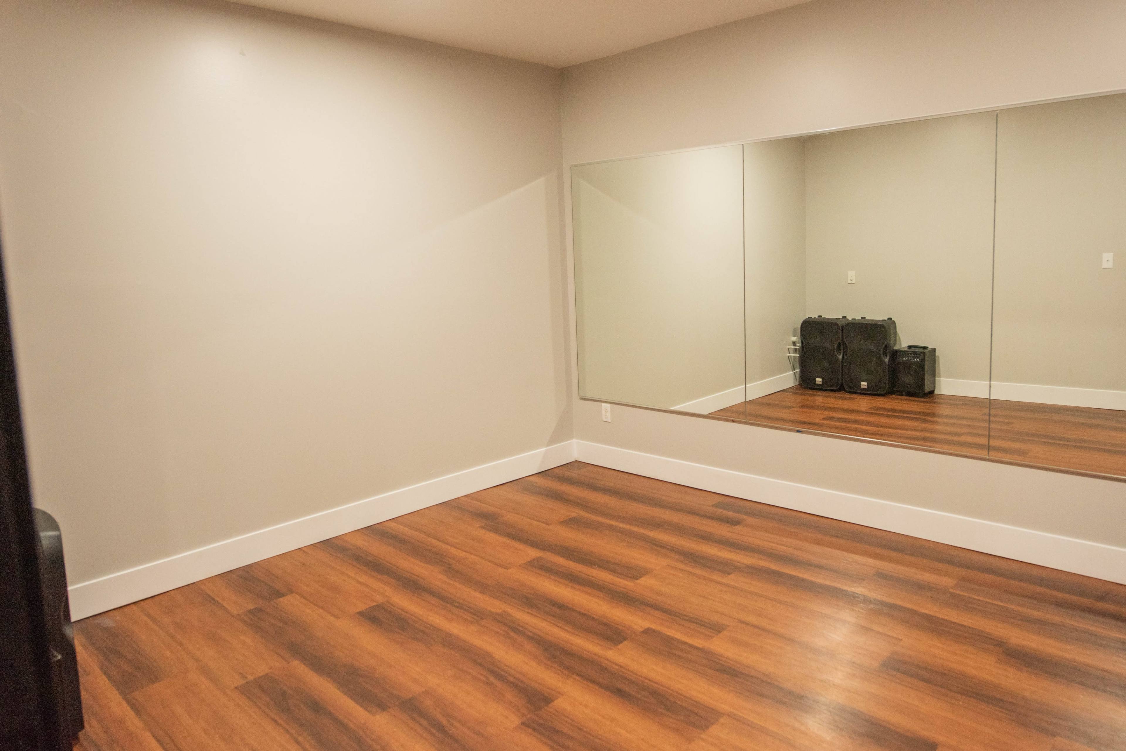 A vacant room with hardwood floors and a large mirror on one wall.