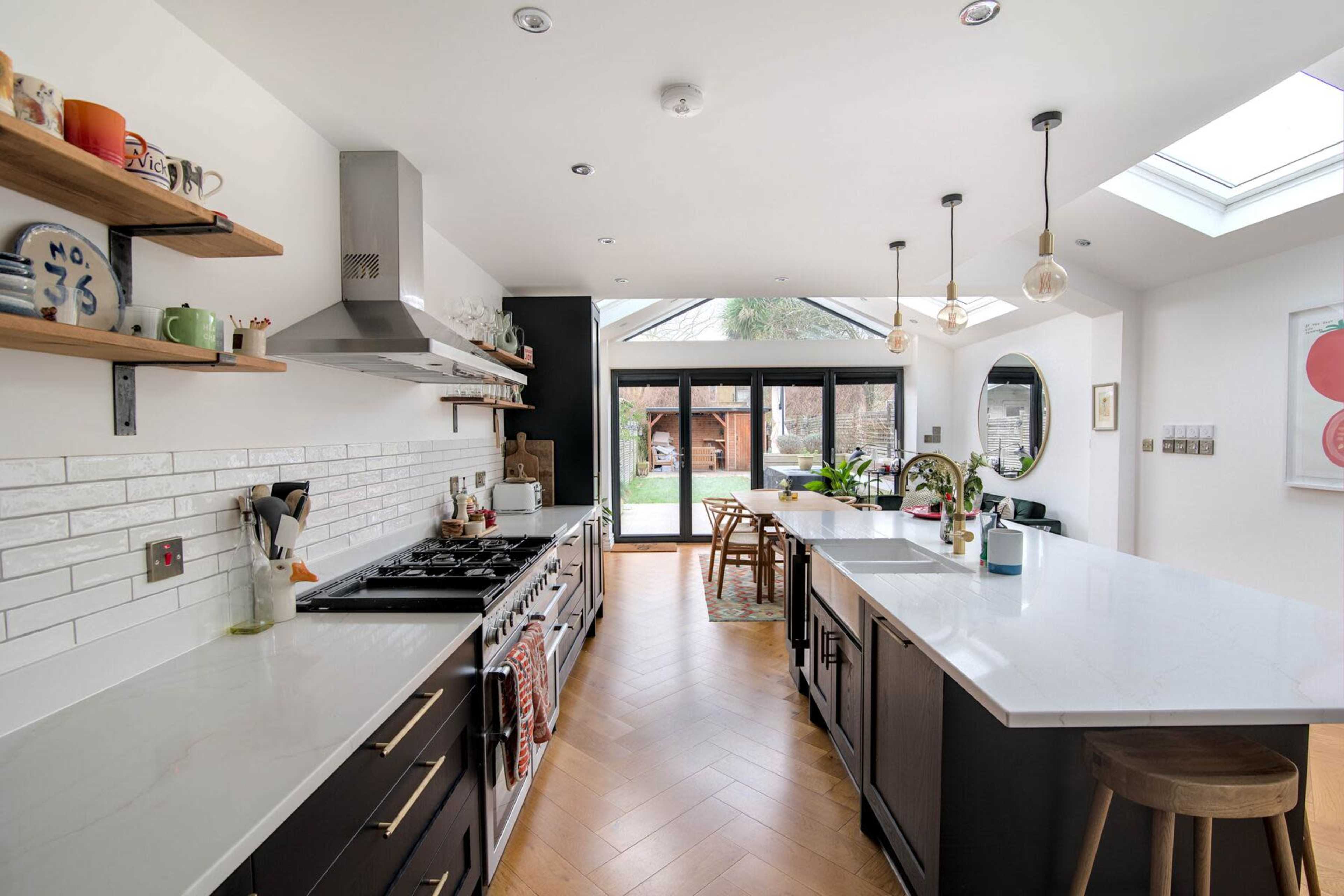 The image shows a modern kitchen featuring an island, sleek cabinetry, and large windows that open to a garden area.