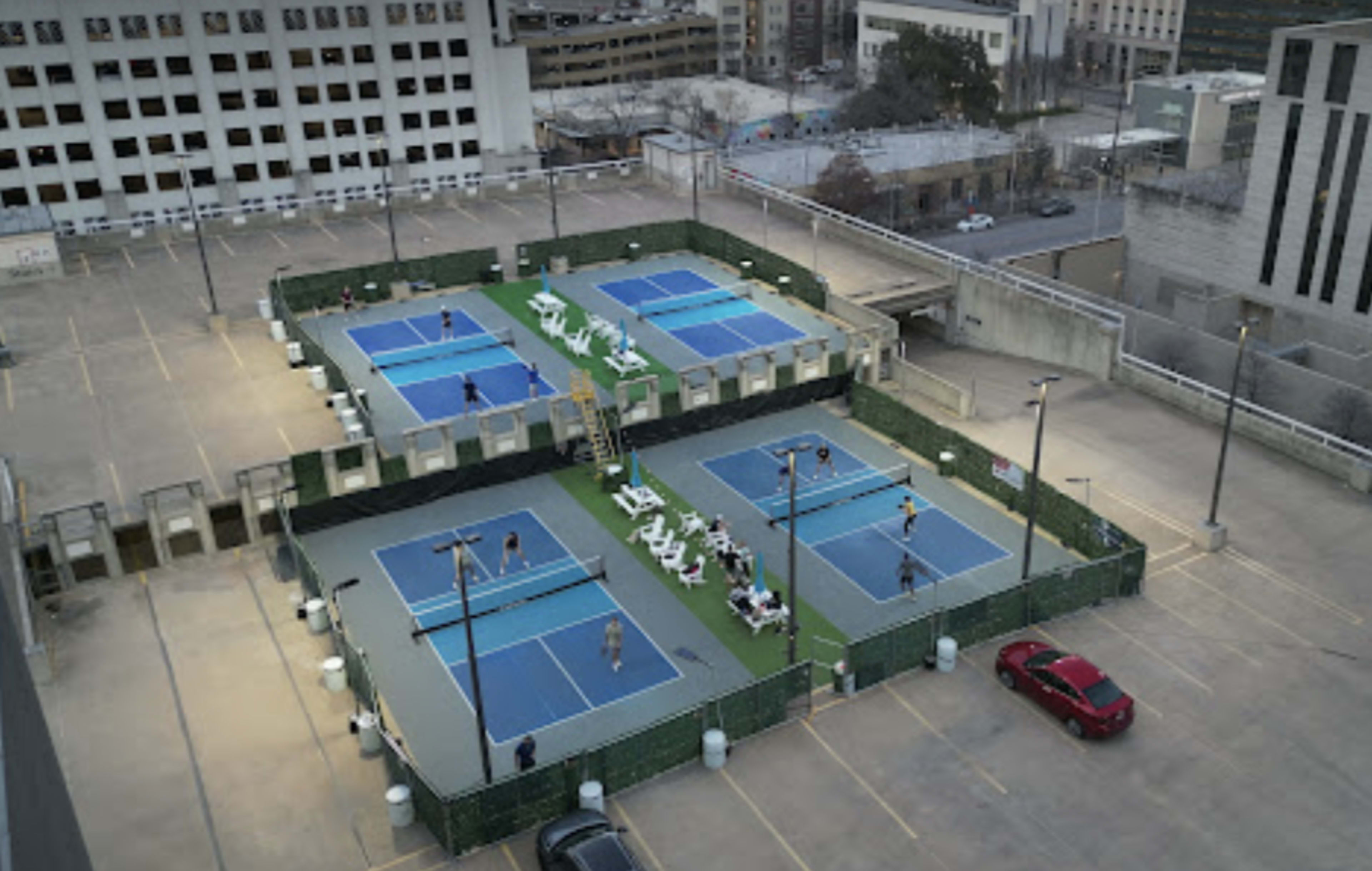 An elevated view of a rooftop tennis facility with multiple courts surrounded by green fencing and players actively participating in games.