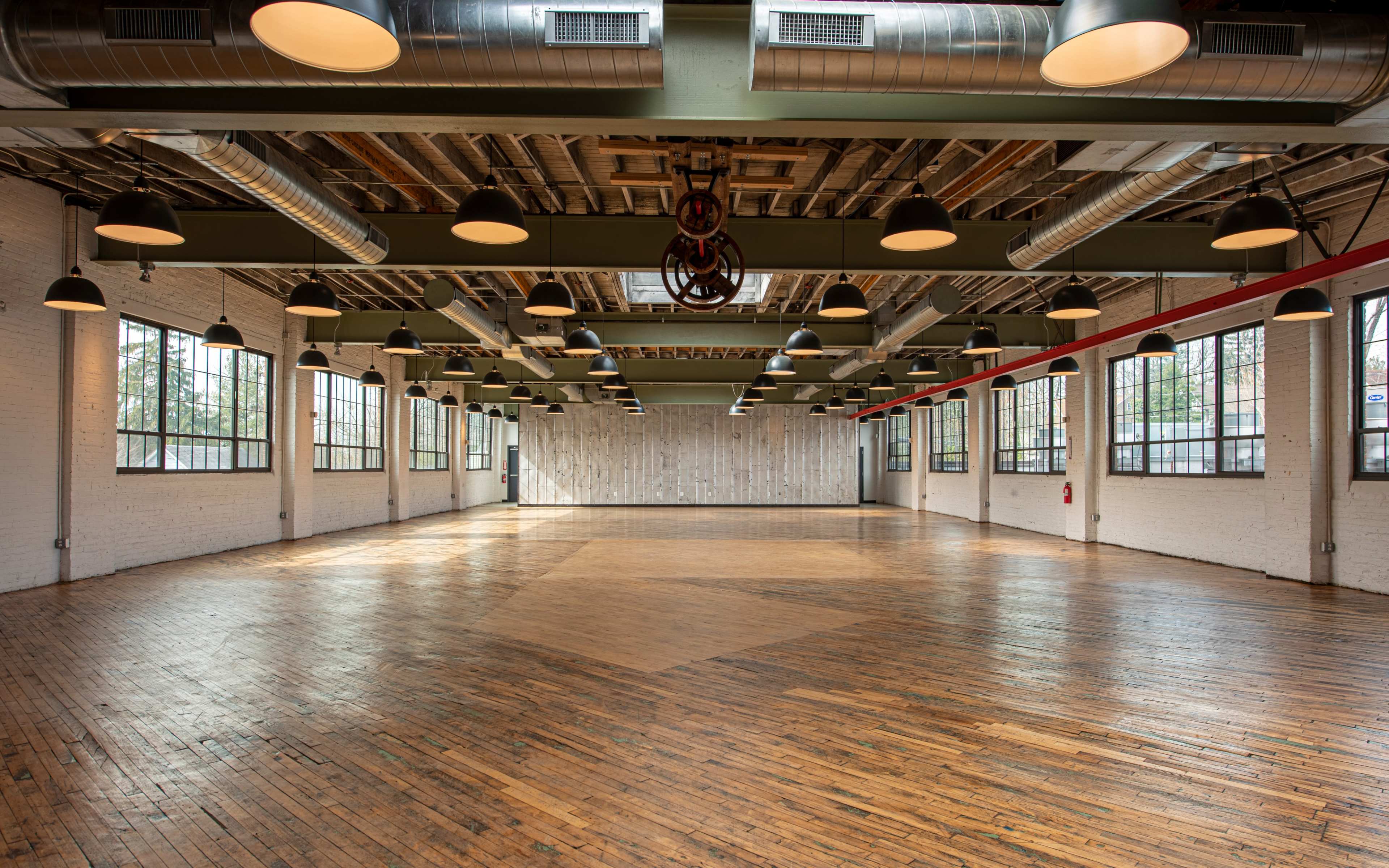 A spacious, well-lit industrial room with large windows and wooden floors, featuring exposed beams and overhead lighting.