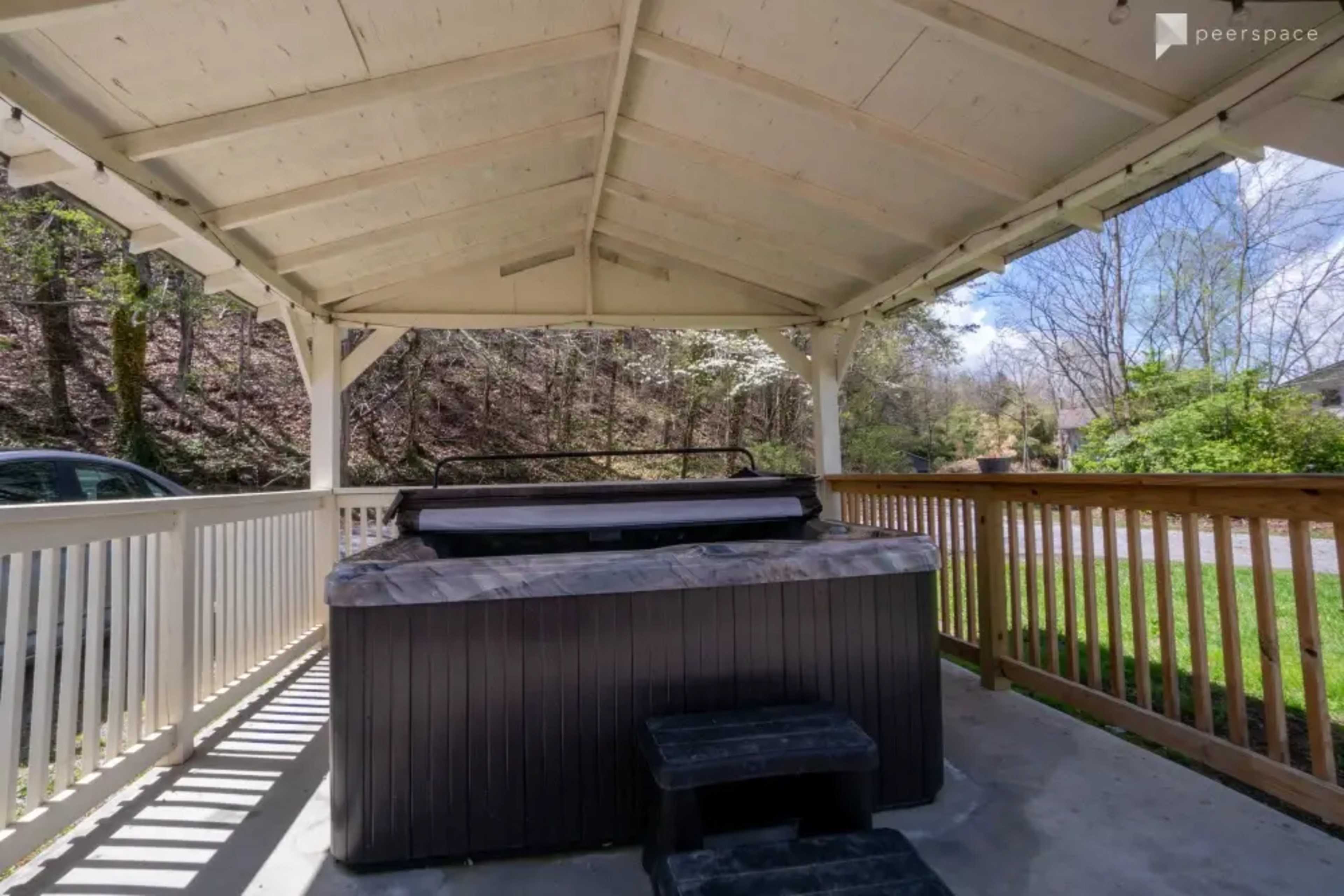A hot tub under a covered gazebo with wooden railings surrounded by trees.