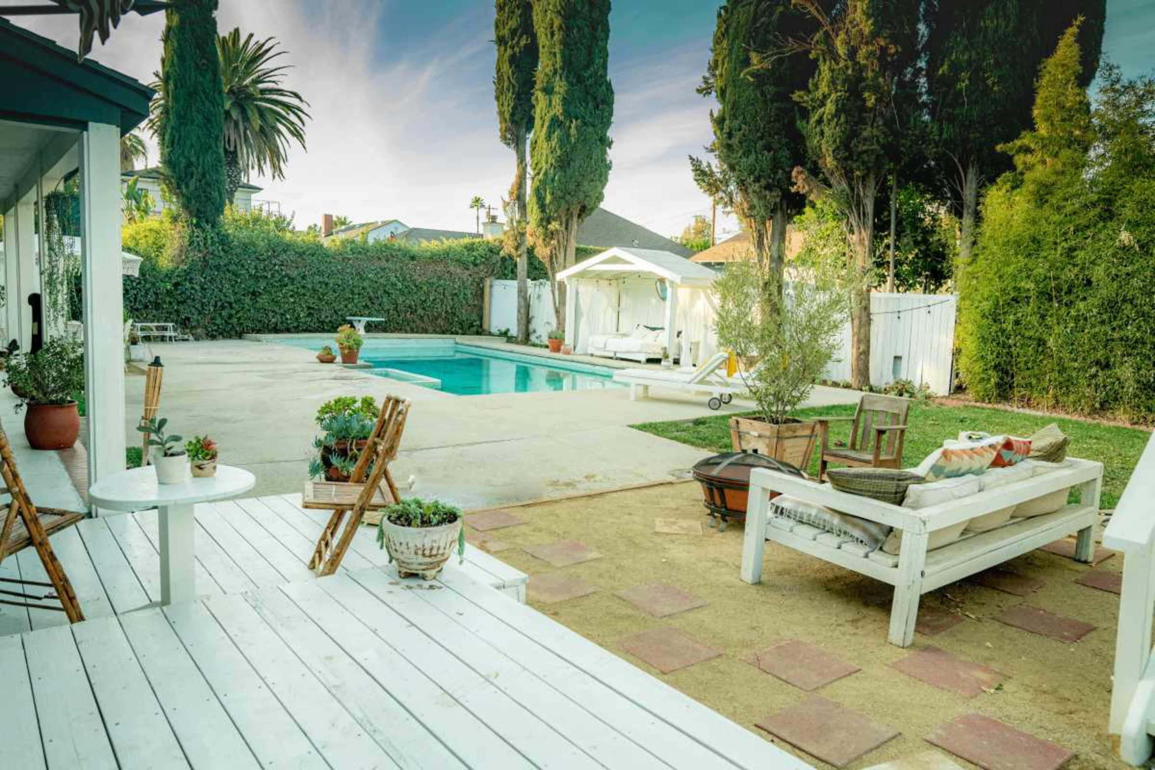 The image shows a backyard with a swimming pool surrounded by seating areas and greenery.