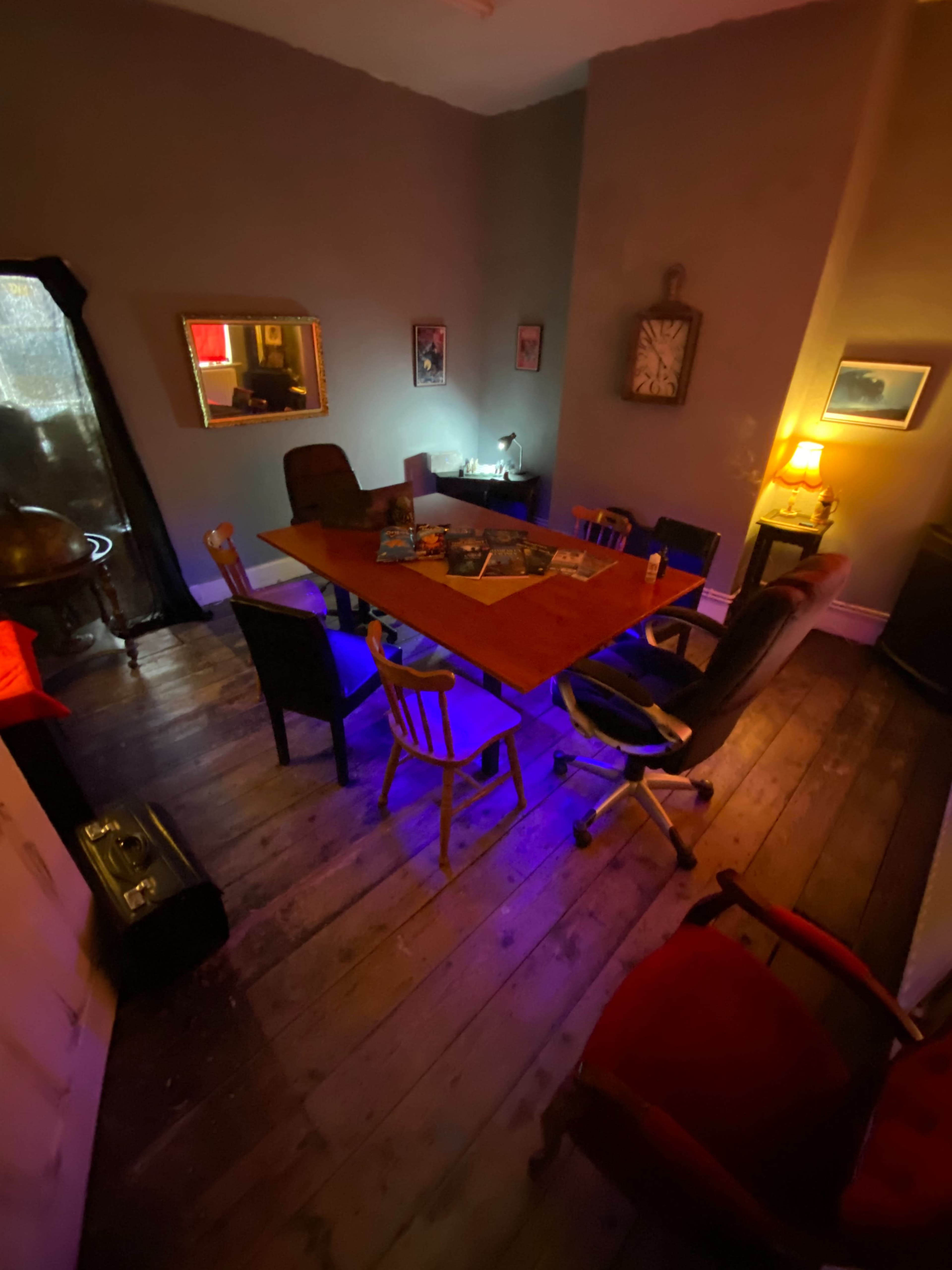 A wooden conference table surrounded by various chairs is set up in a dimly lit room with a clock and wall decorations.