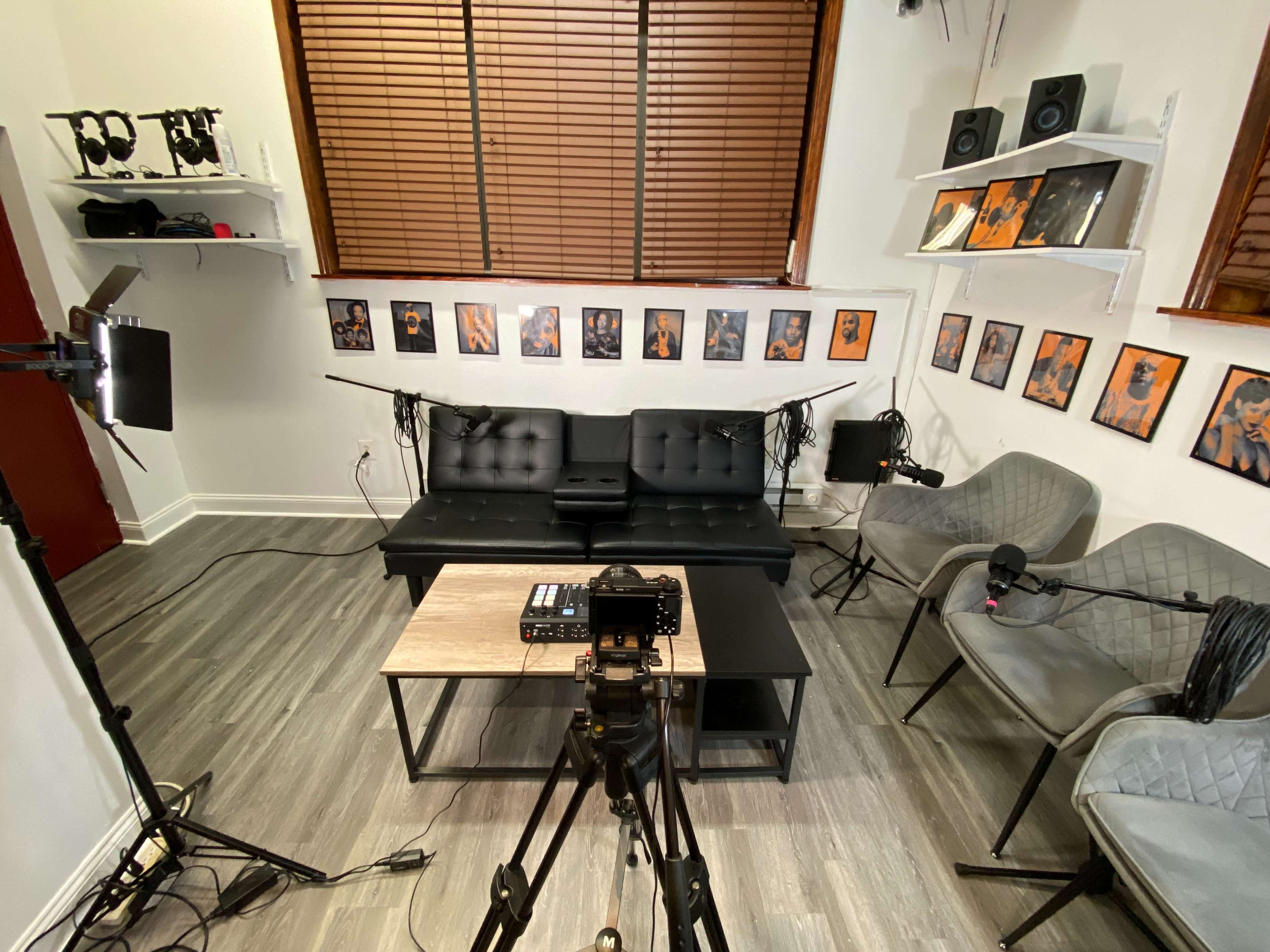 The image shows a video recording setup in a room with a black couch, two gray chairs, a wooden coffee table, and several framed pictures on the walls.