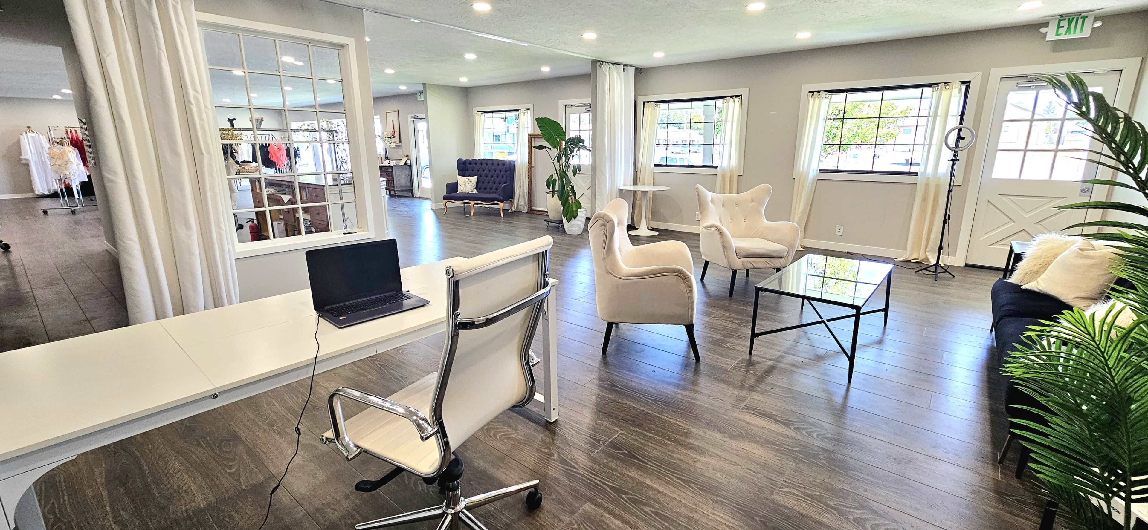 A modern interior space with a desk, chairs, and a coffee table, featuring large windows and light-colored walls.
