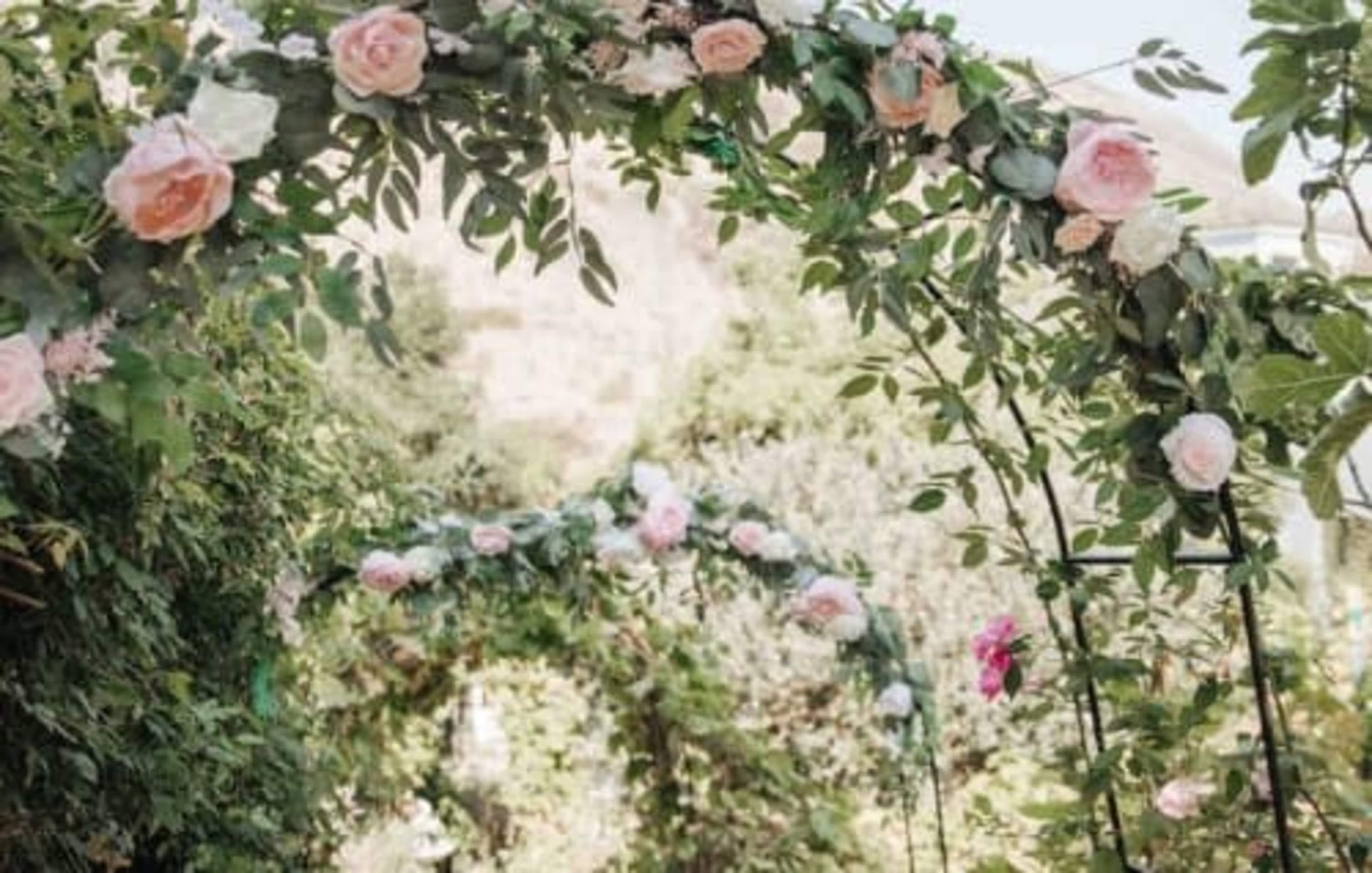 The image shows a garden pathway adorned with floral arches featuring pink roses and greenery.