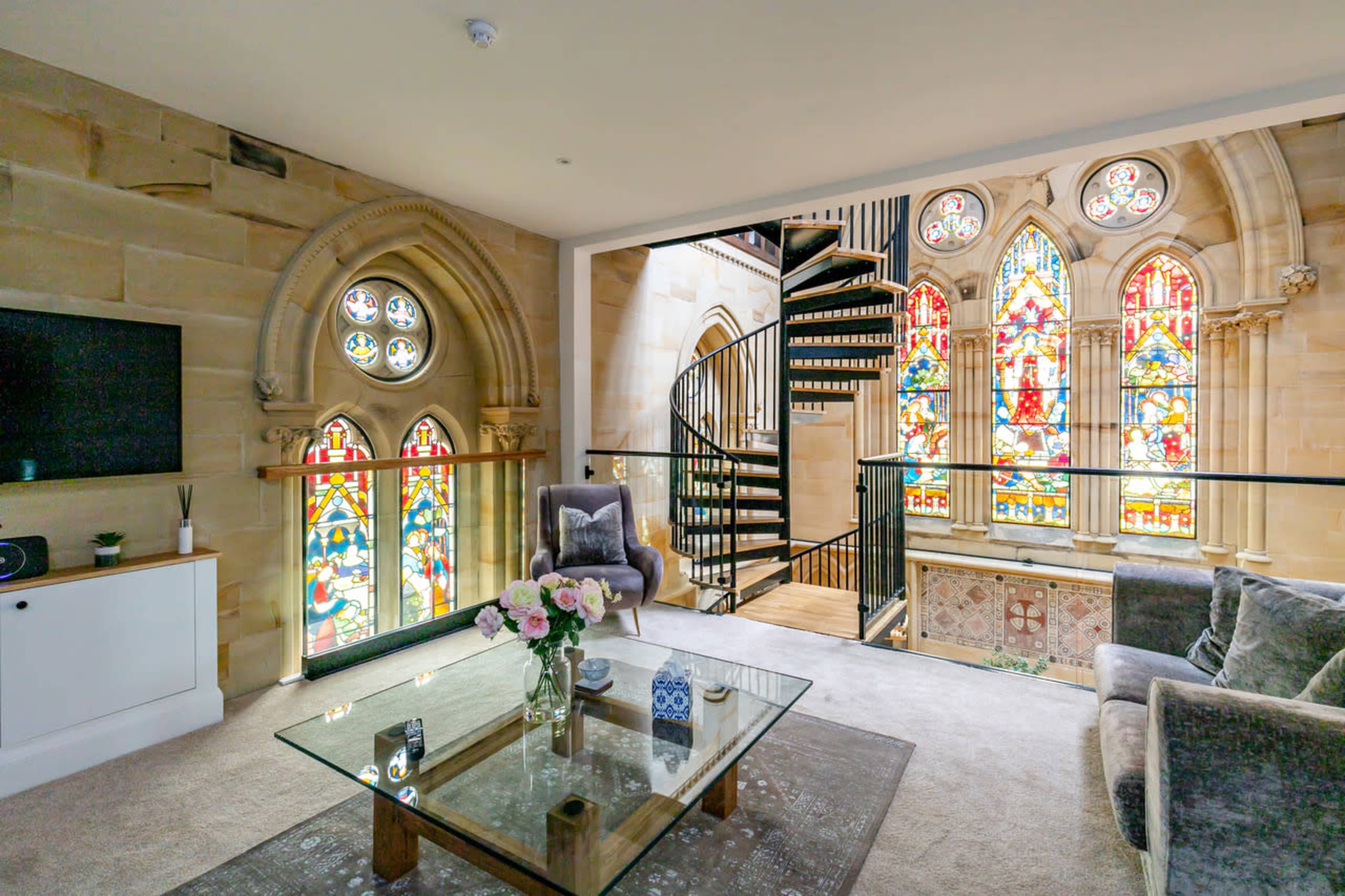 A spacious living area featuring ornate stained glass windows and a spiral staircase leading to the upper floor.