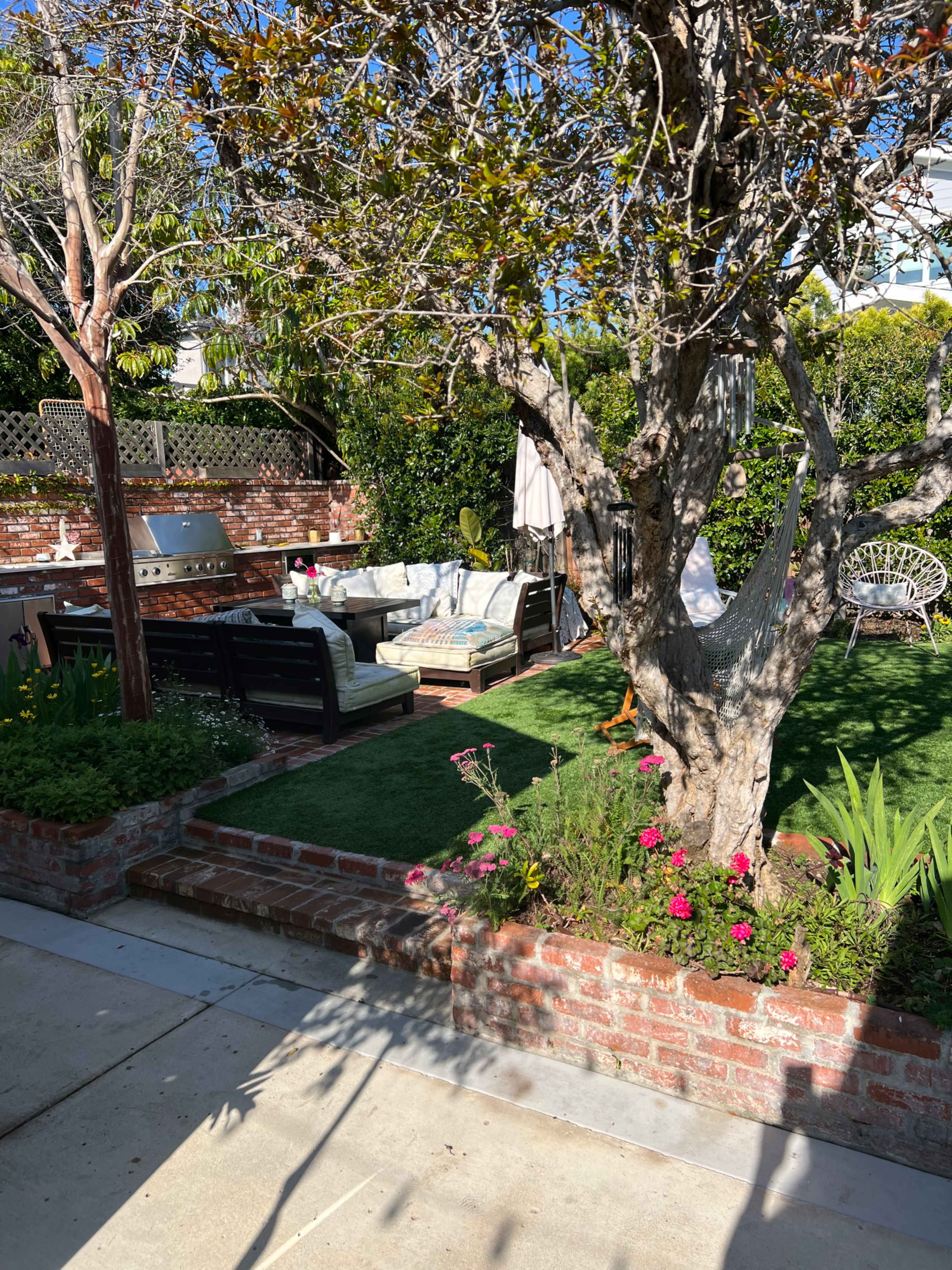 A landscaped backyard with a seating area, a barbecue grill, and flower beds surrounding a grassy lawn.