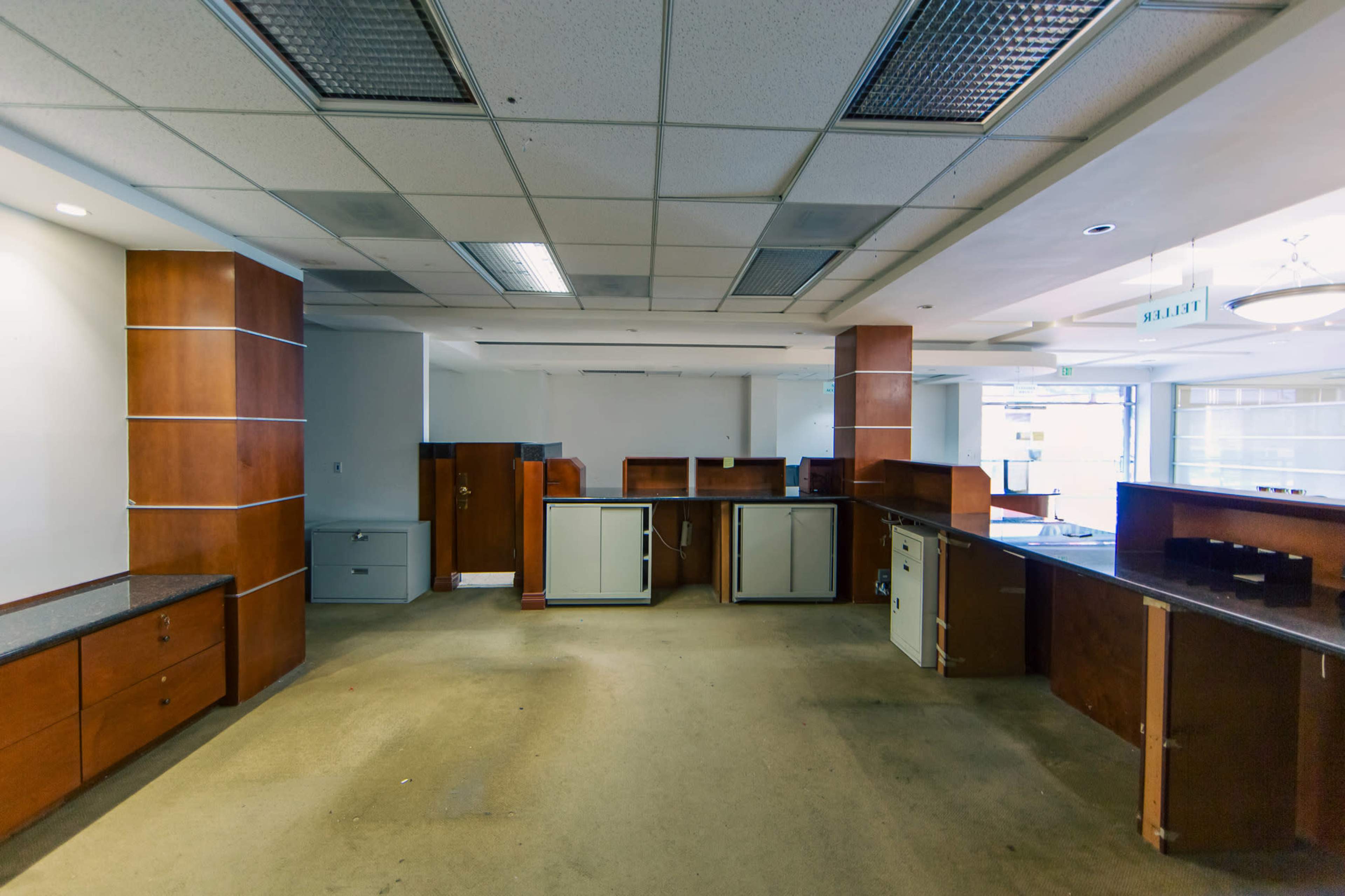 An empty office space features wooden cabinets and counters with a carpeted floor and fluorescent lighting.
