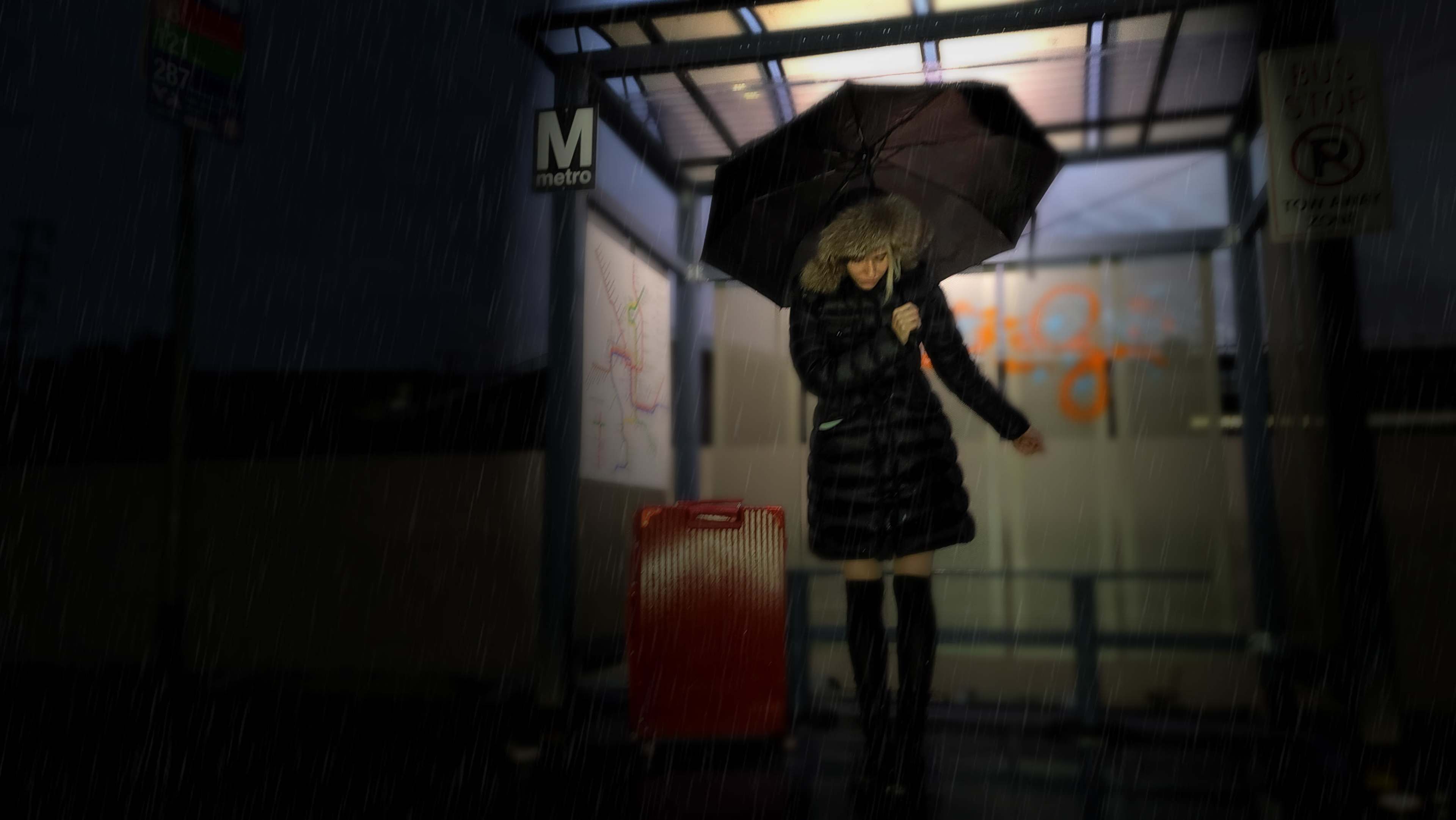 A person in a dark coat stands under a bus stop shelter, holding an umbrella while rain pours around them.