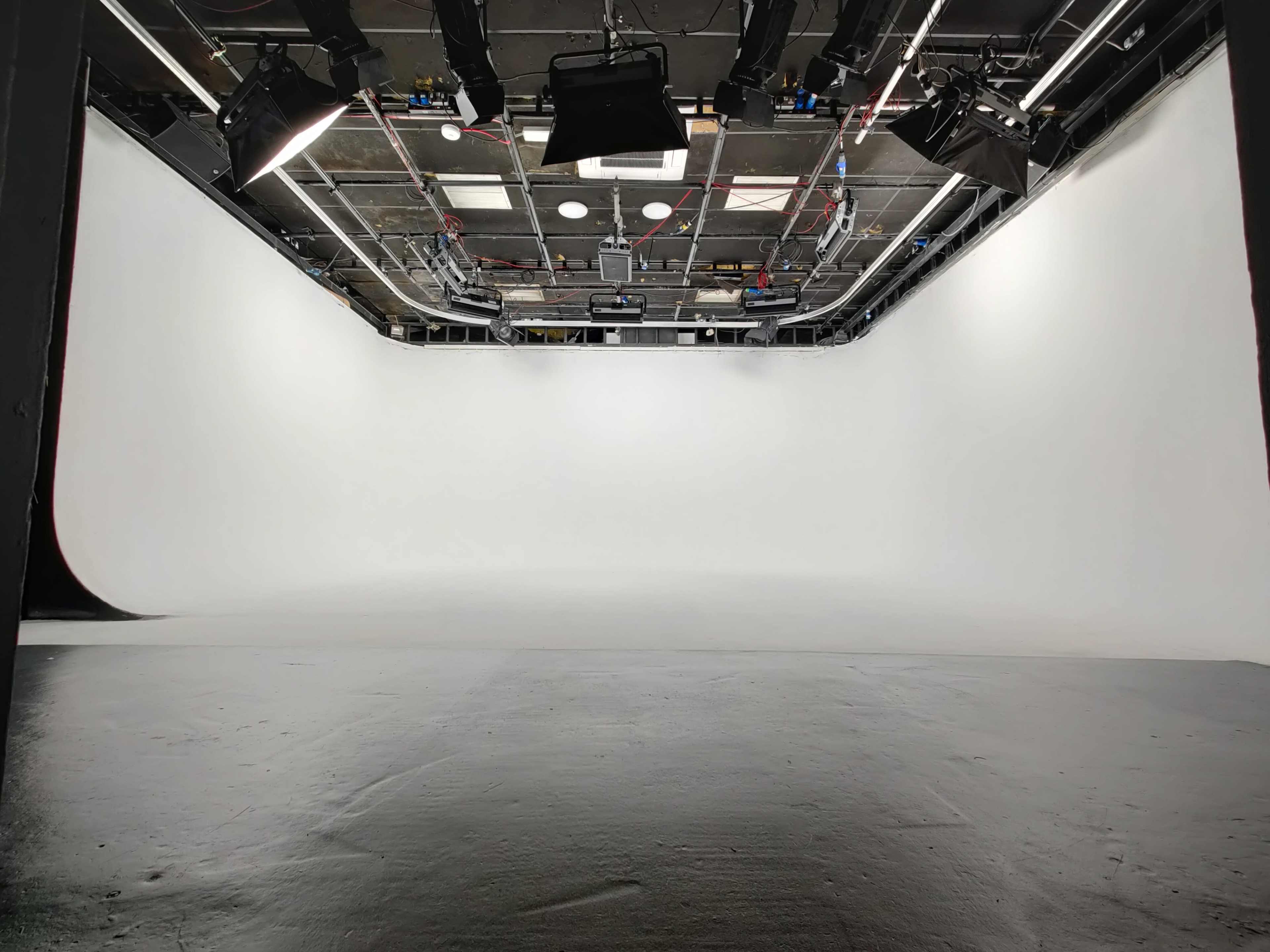 A spacious photography studio with a seamless white backdrop and studio lighting overhead.