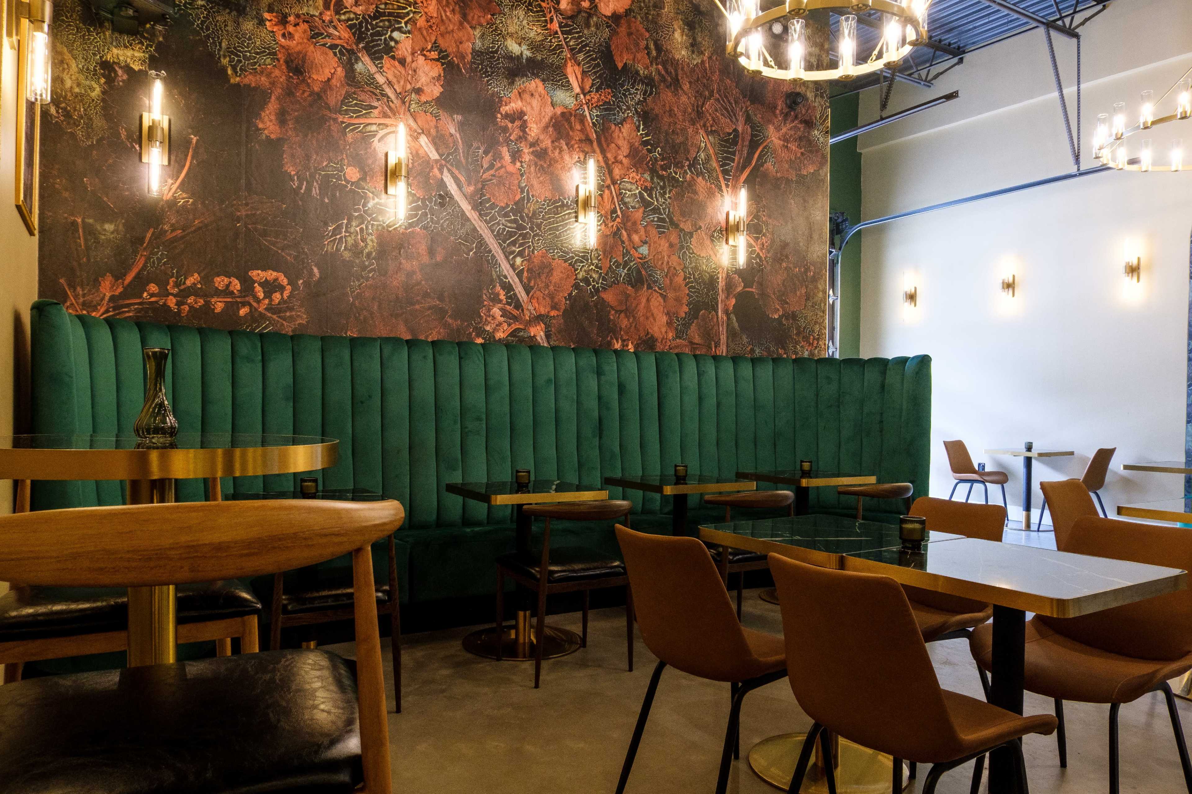The image shows a stylish café interior with a green upholstered banquette, wooden tables, and modern lighting on the walls.