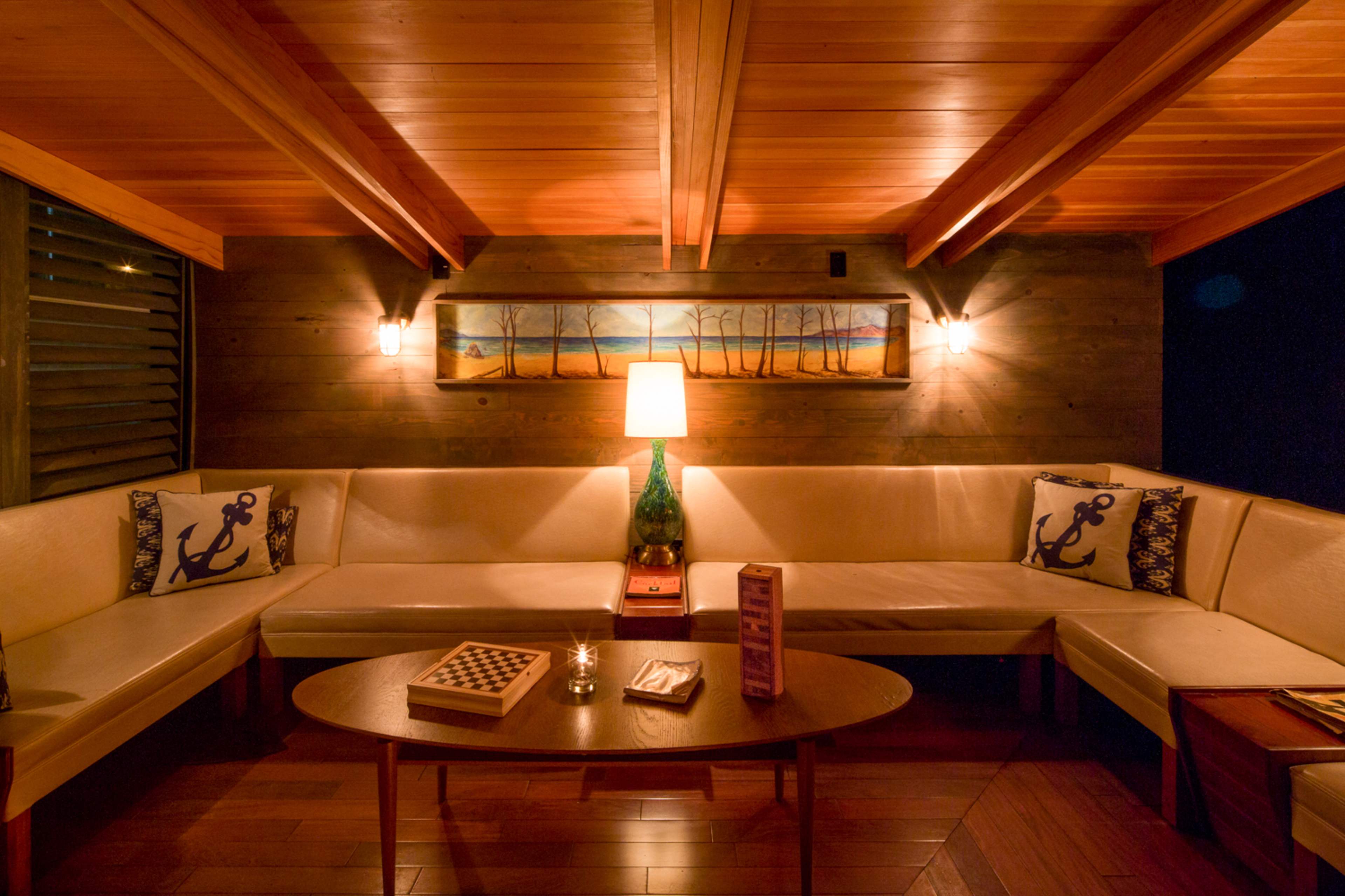A cozy indoor seating area features a sectional couch with decorative pillows, a wooden table, and a lamp illuminating a wall art piece above.