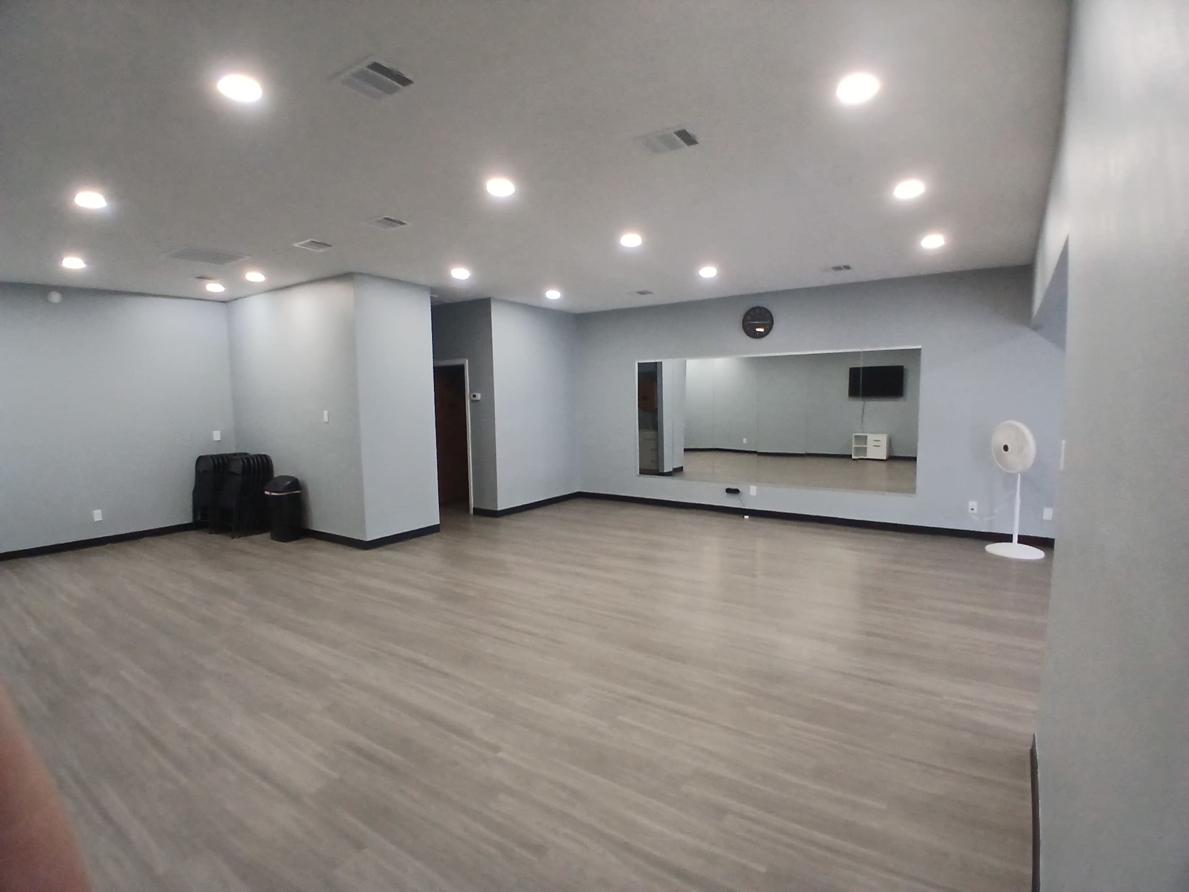 The image shows a spacious, empty room with gray walls, a large mirror, and recessed lighting.