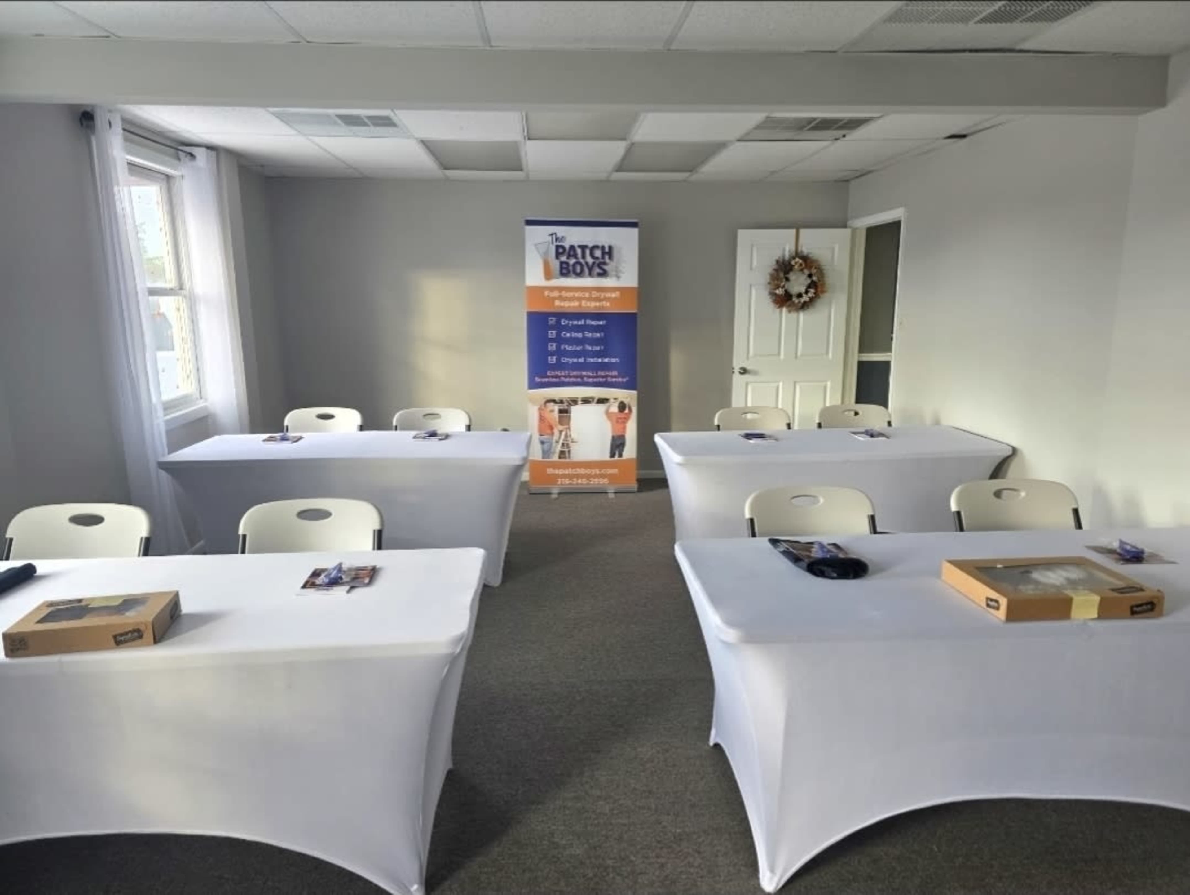 The image shows a training room with several tables covered in white tablecloths, two windows, and an informational banner for "The Patch Boys" in the background.