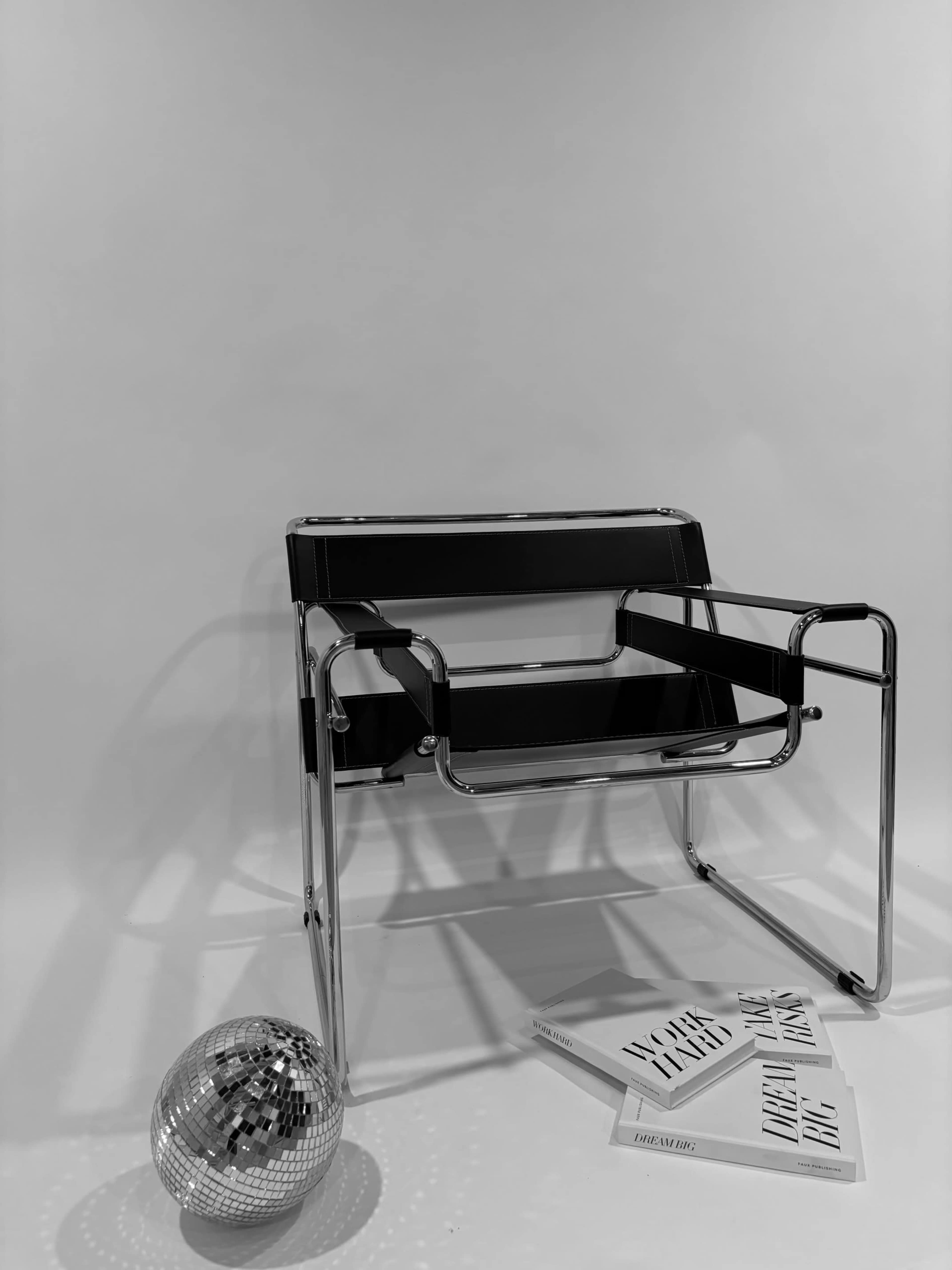 A black and chrome modern chair positioned beside a disco ball and several books on a light background.