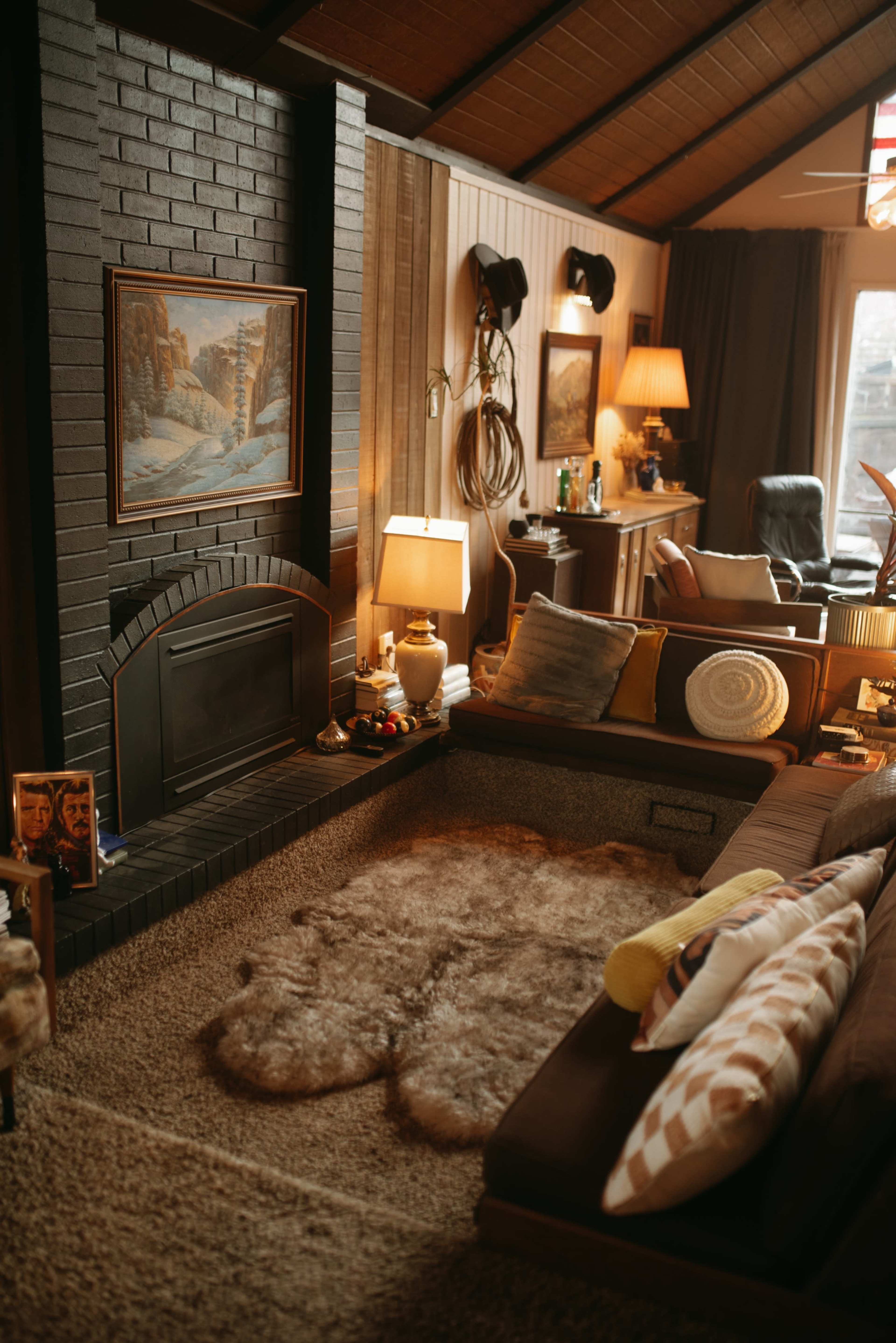 The image shows a cozy living room featuring a sunken seating area with a plush rug, a fireplace, and wooden paneling on the walls.
