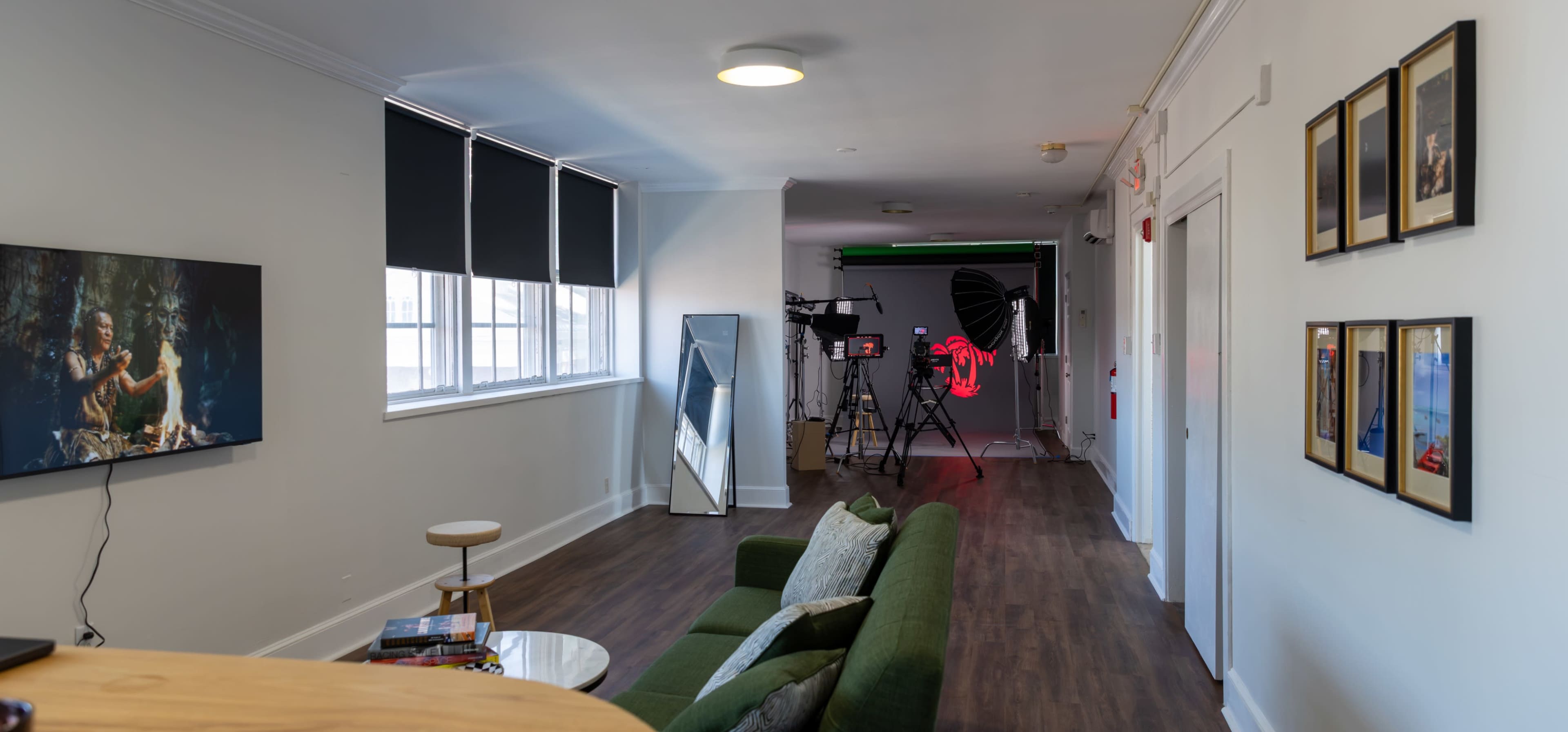 The image shows a modern interior hallway with a green backdrop setup for photography, a couch, and a television displaying an image on one wall, while framed photos hang along another wall.