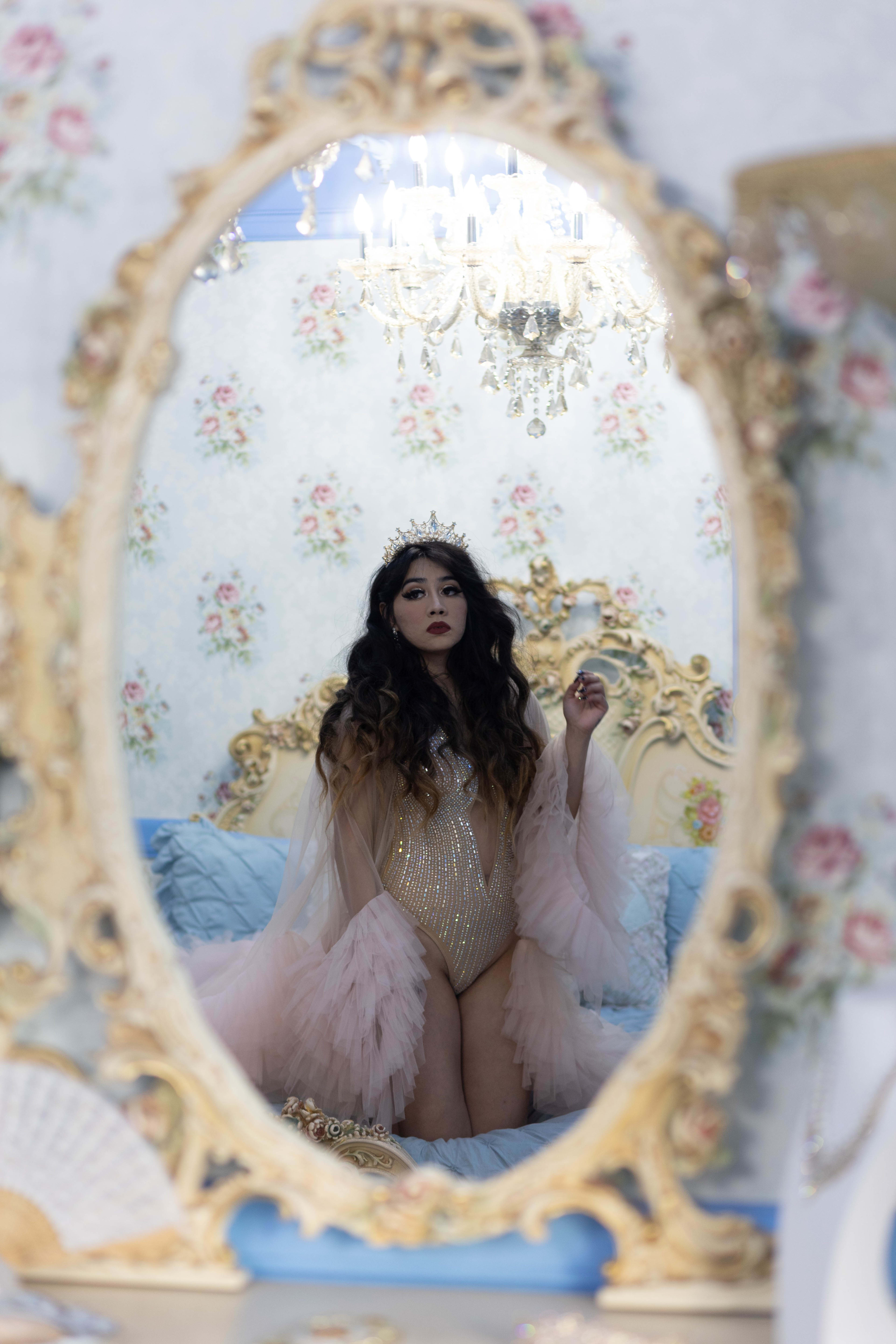A woman dressed in princess-themed clothing posing for a photoshoot in front of a gold-framed mirror.