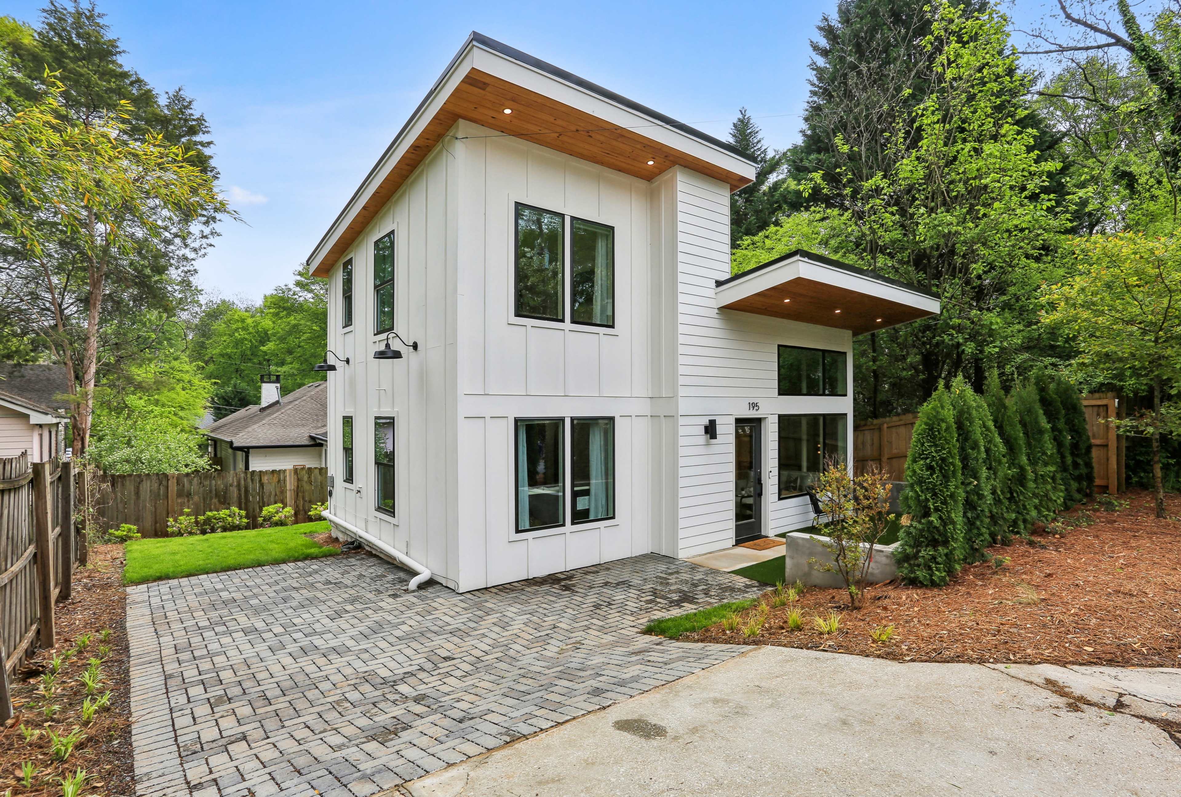 A modern two-story house with large windows, a covered entrance, and a stone driveway surrounded by greenery.