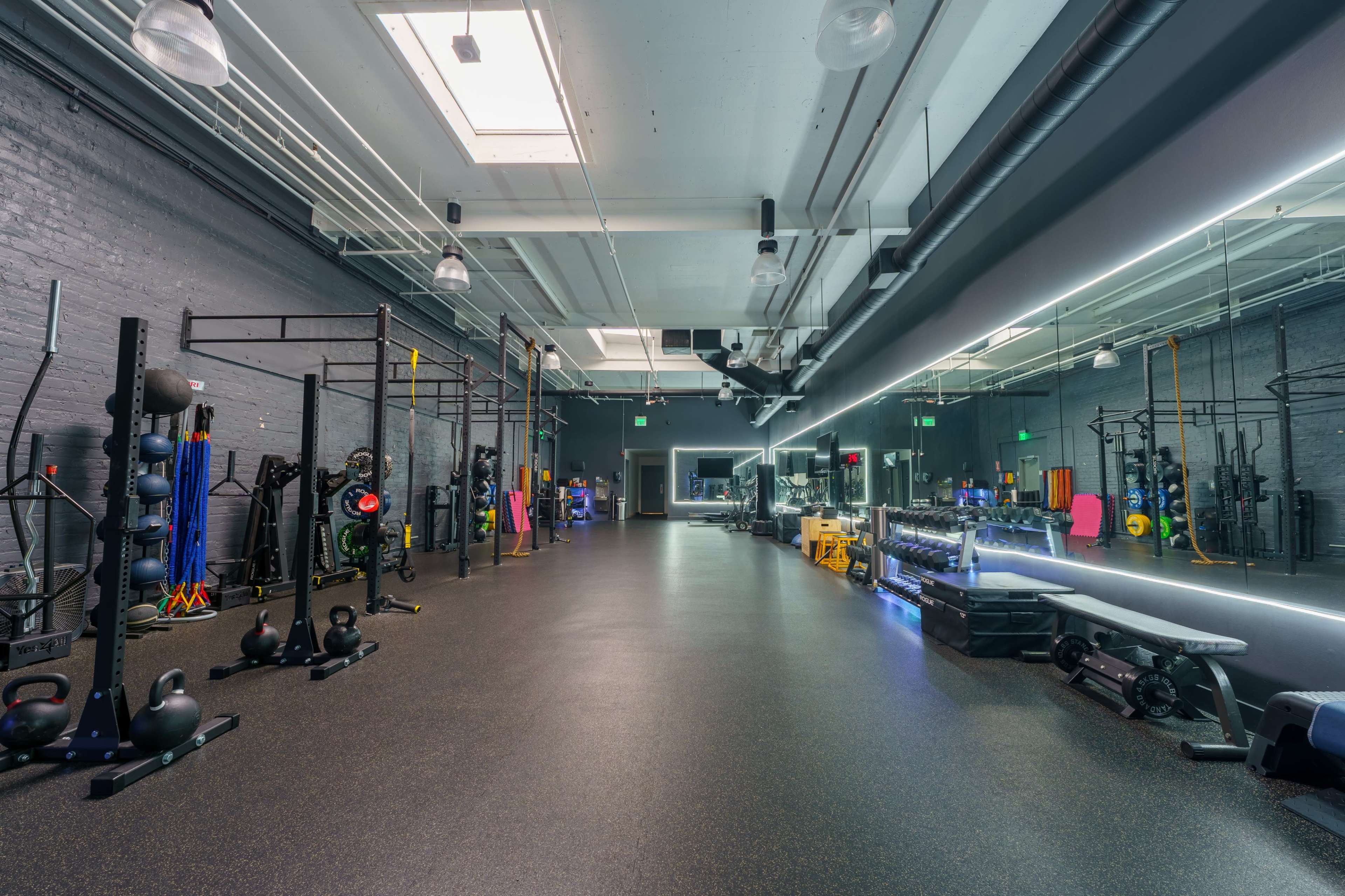 The image shows a spacious, well-equipped gym with various fitness equipment and exercise stations arranged along the walls.