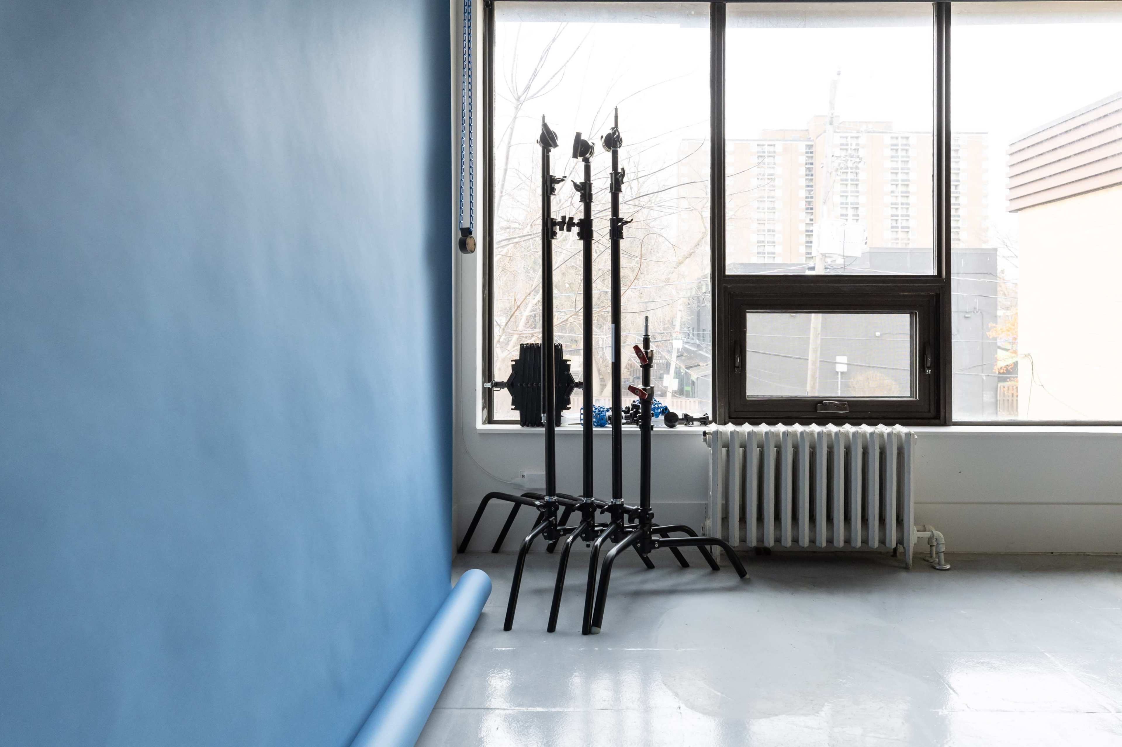 A room features a blue wall and a window with three black light stands positioned near the radiator.