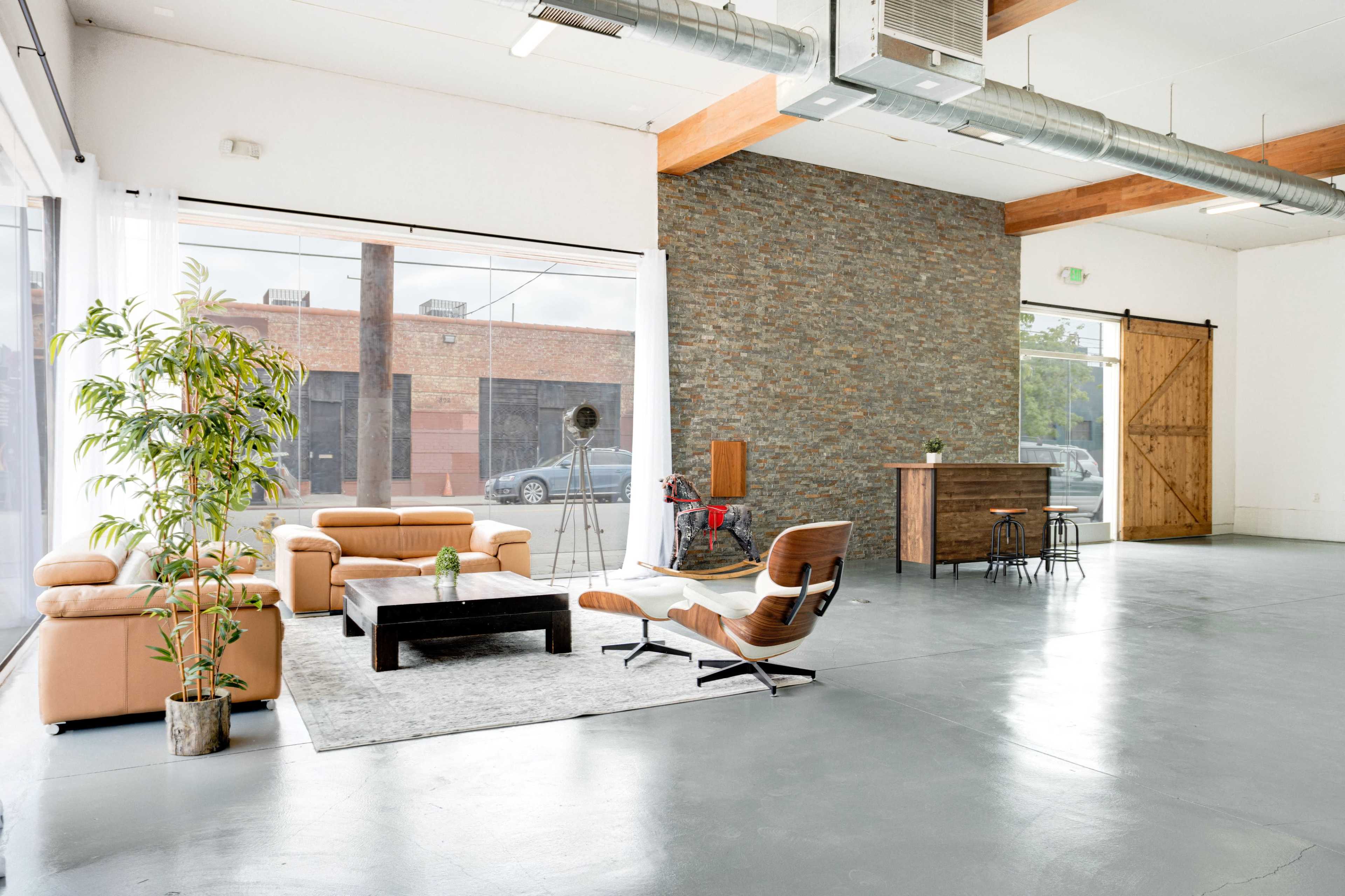 A spacious interior featuring a seating area with a tan leather sofa, a wooden bar, a decorative plant, and large windows that open to an outdoor view.