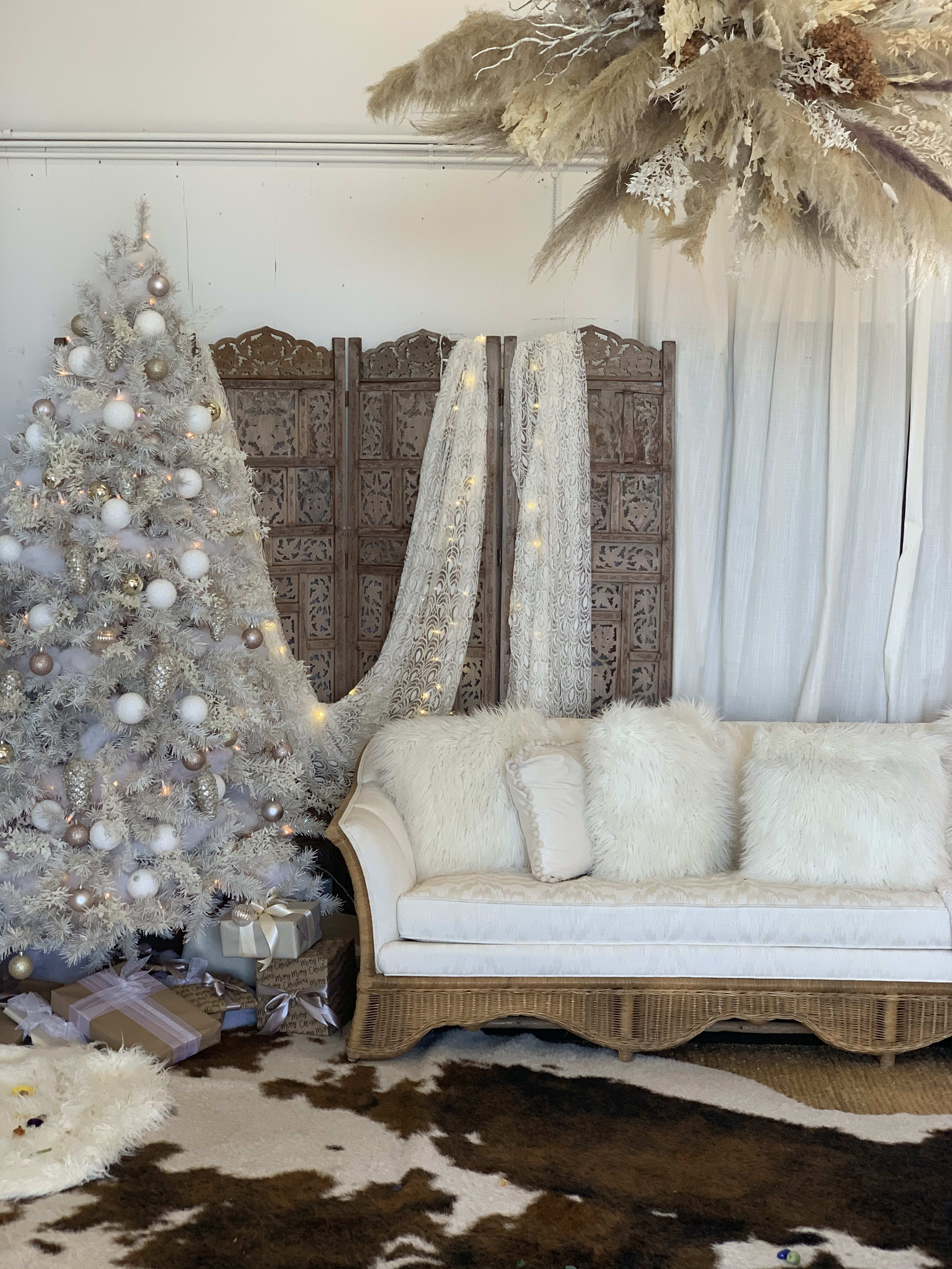 A boho white couch adorned next to a Christmas tree for a photoshoot.