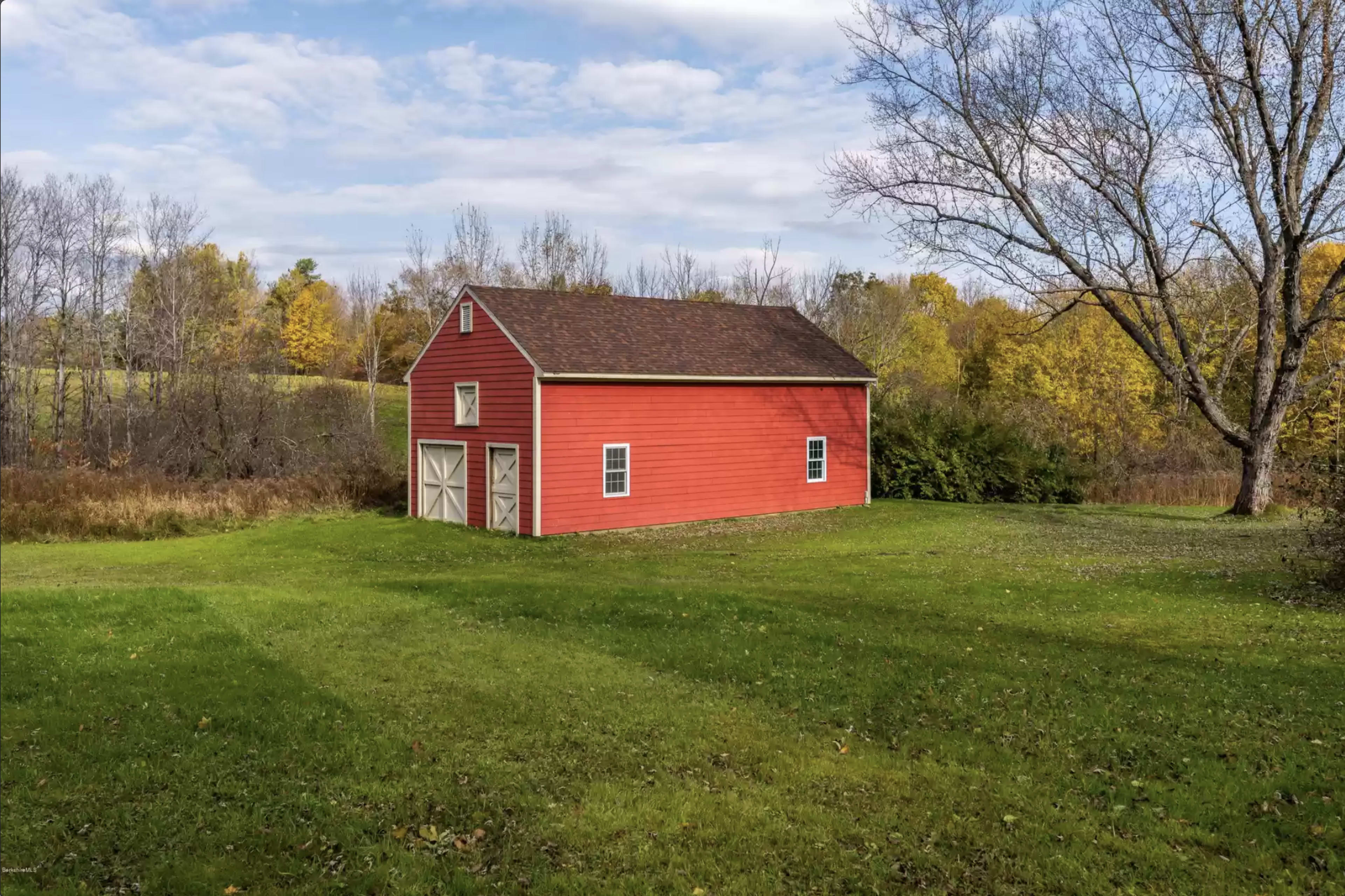 A red barn situated on a grassy area, surrounded by trees and open farmland.
