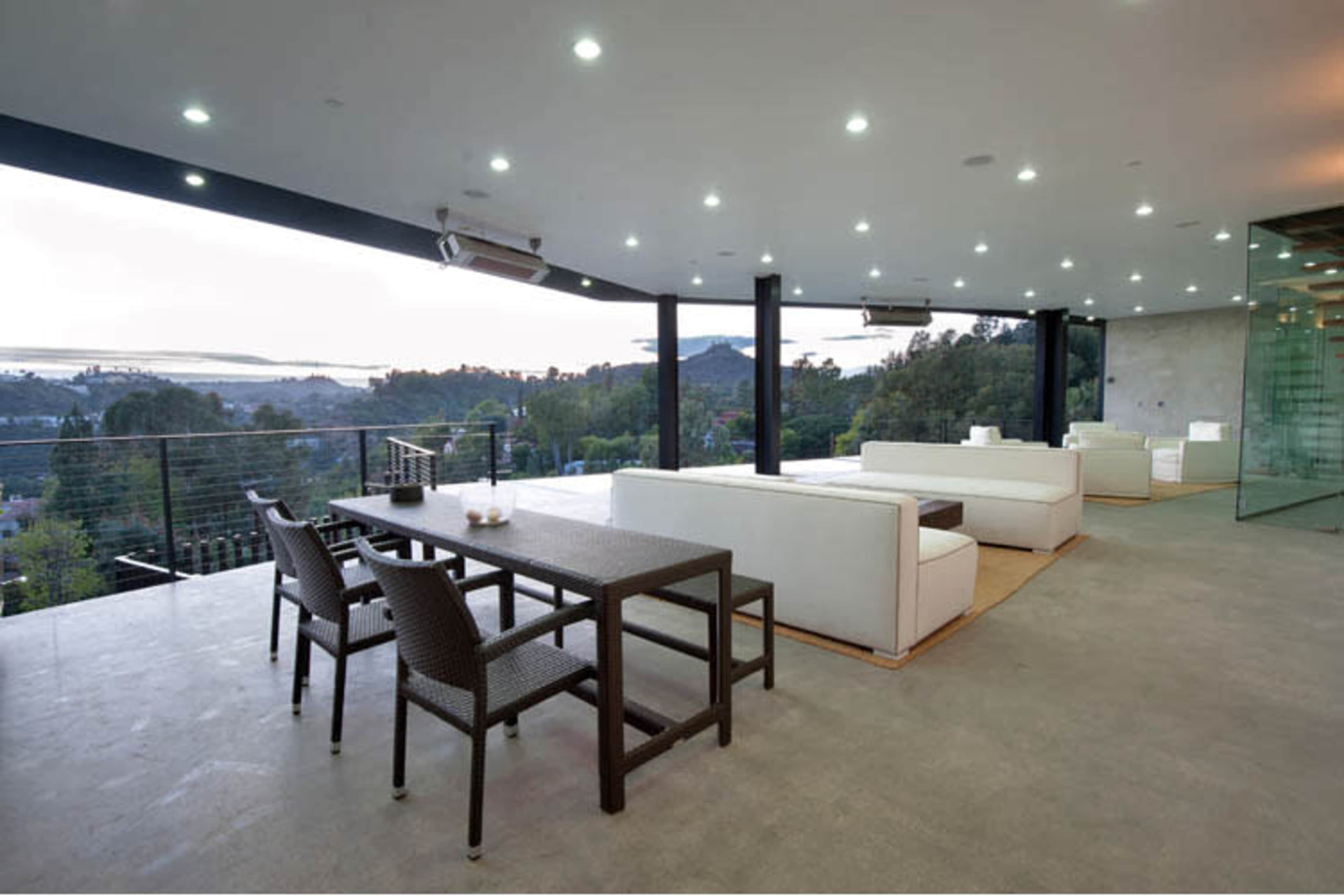 The image depicts a modern, spacious living area with white furniture and large glass windows overlooking a scenic landscape.