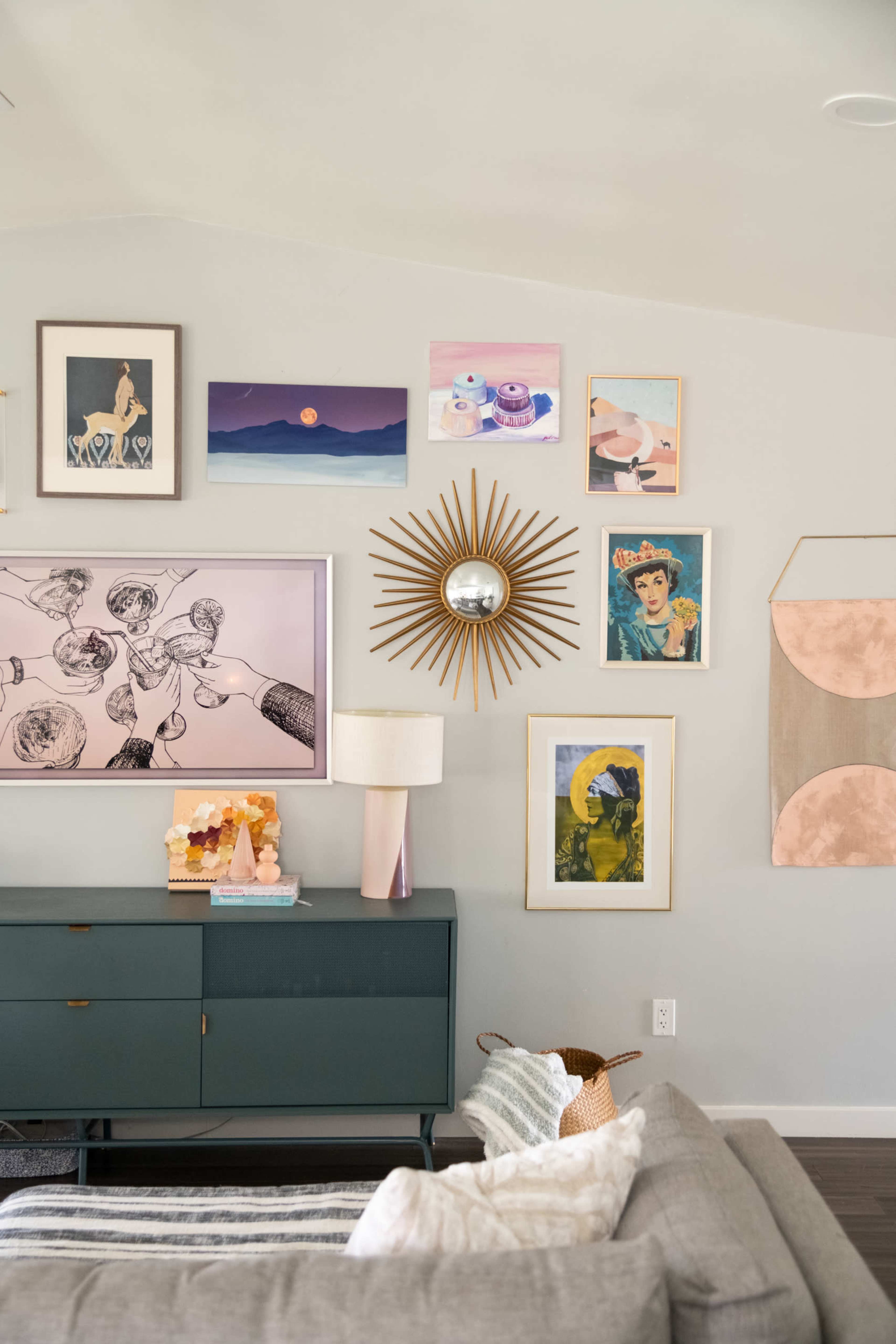 A living room features a green sideboard with decorative items and a wall adorned with various framed artworks and a sunburst mirror.
