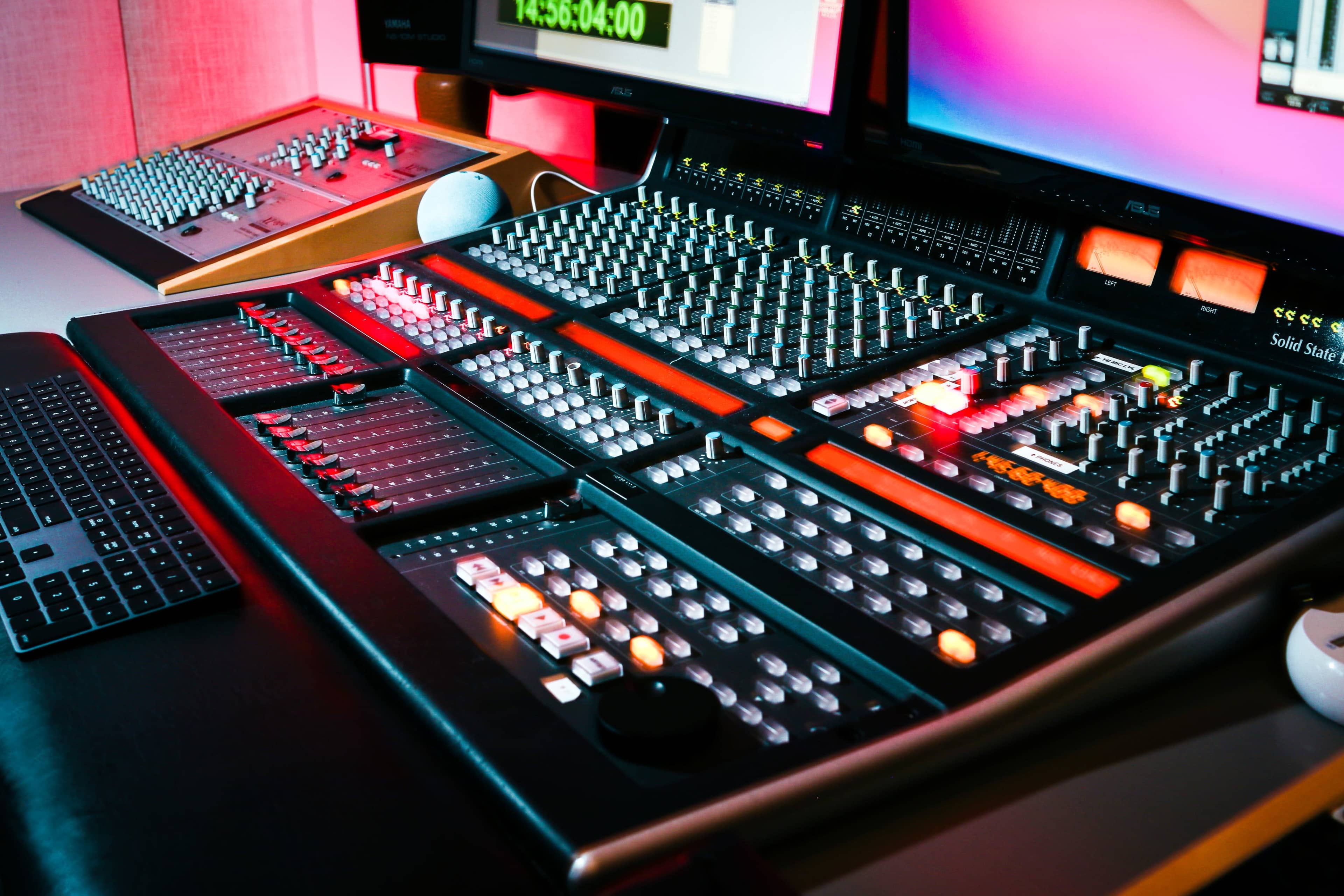 A digital audio mixing console with various controls and screens is prominently displayed in a studio setting.