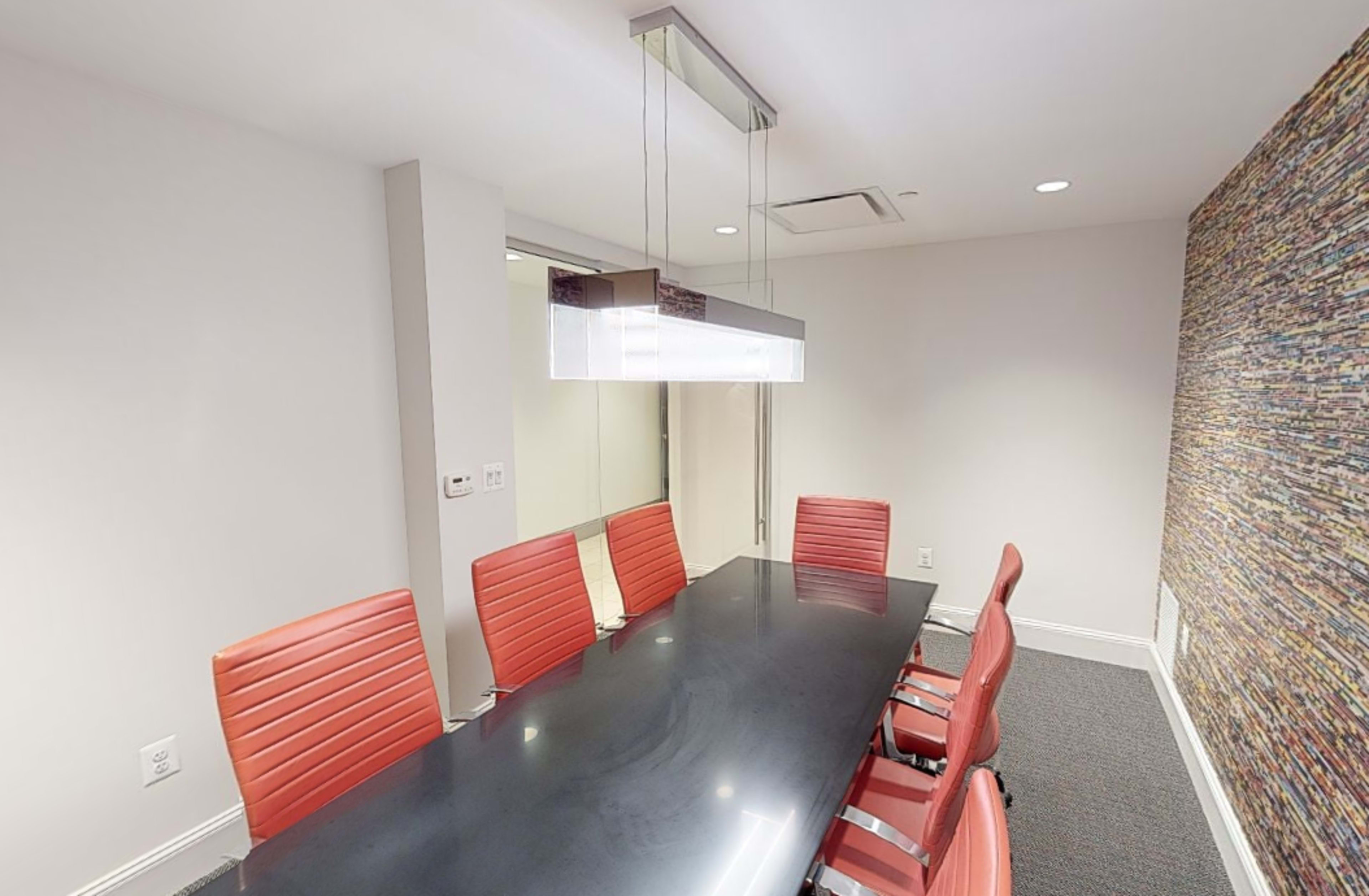 A modern conference room features a long black table with red chairs and overhead lighting.