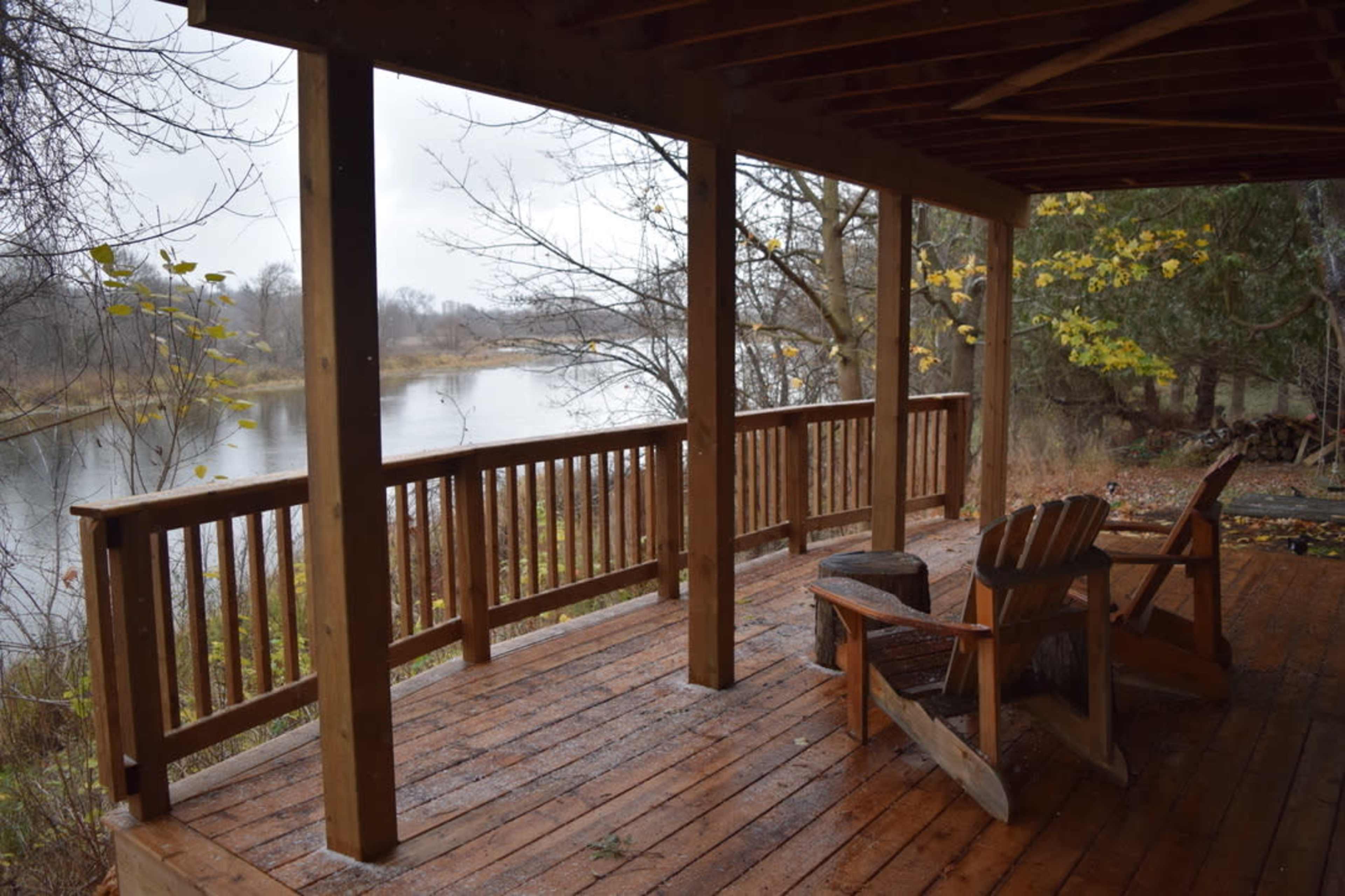 A wooden deck with two chairs overlooks a calm river surrounded by bare trees and autumn foliage.