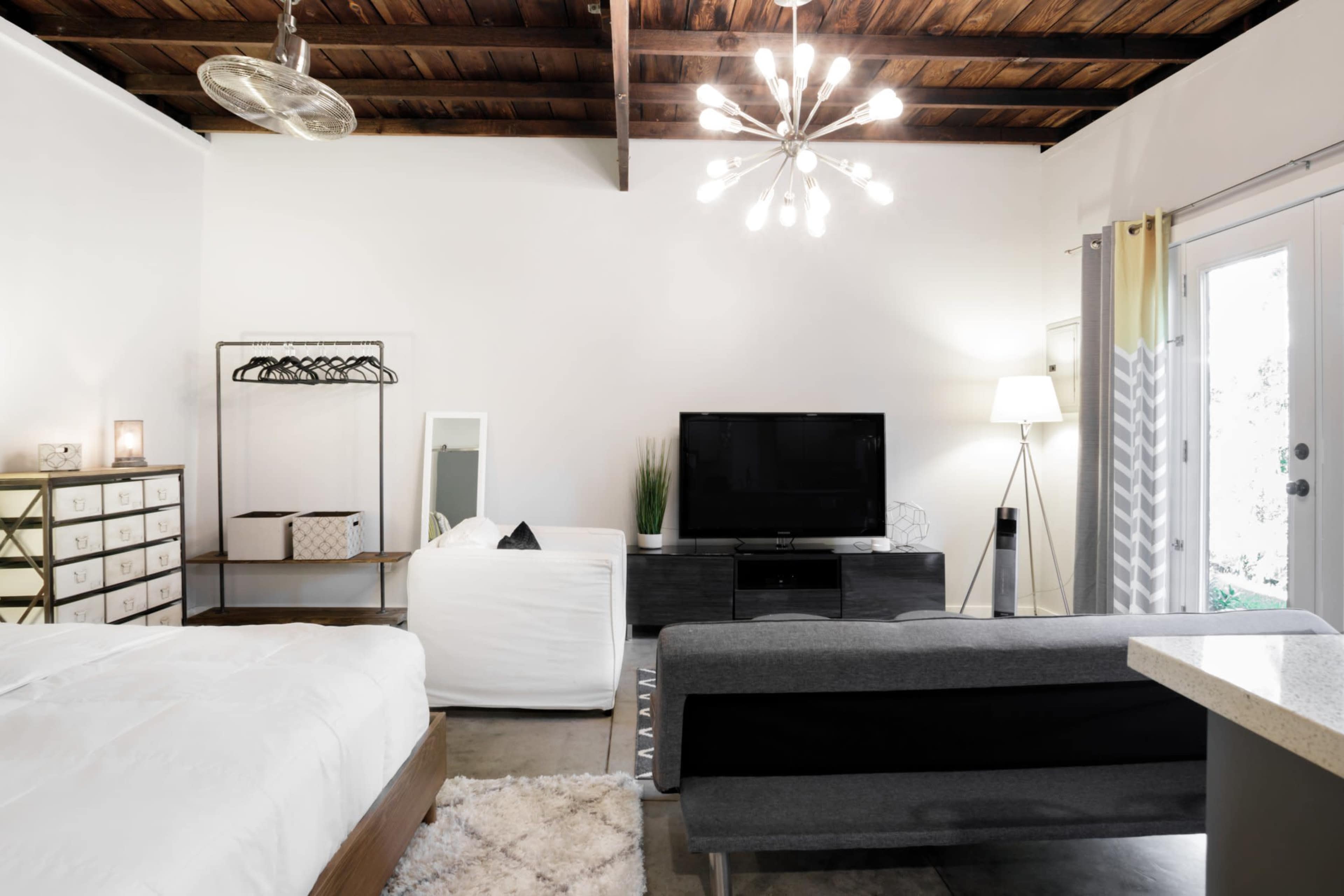 A modern, open living space features a bed, a television, a light fixture, and a seating area with a sofa and decorative elements.