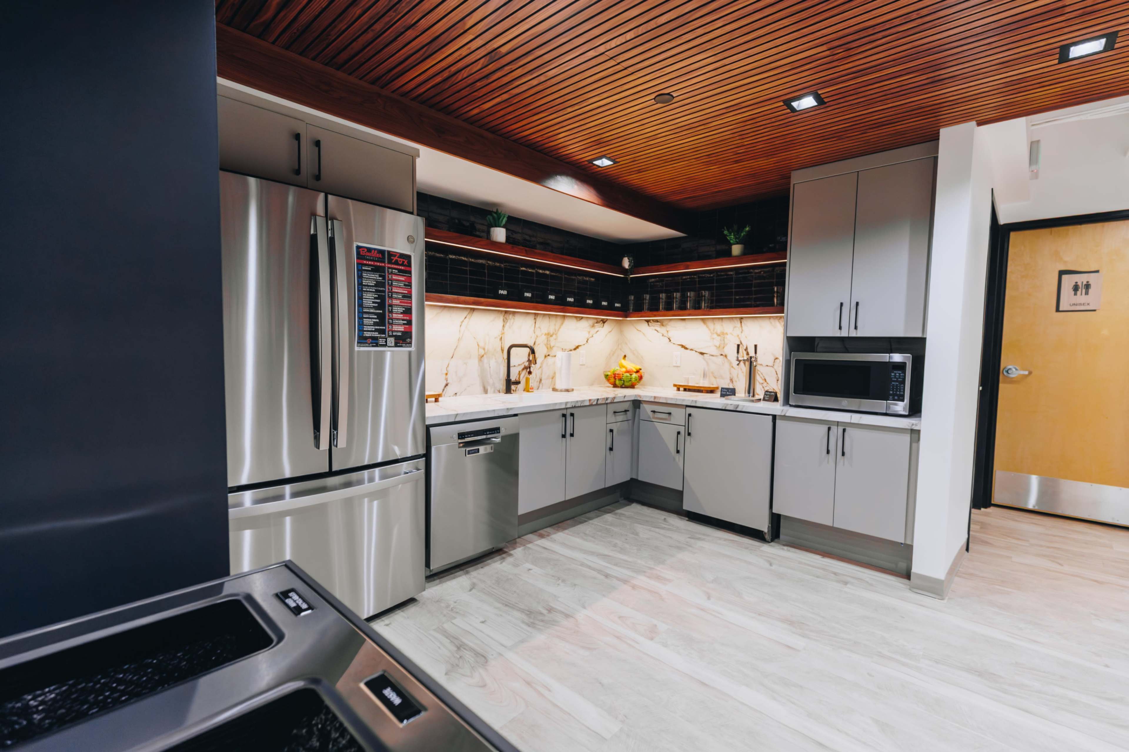The image shows a modern kitchen featuring stainless steel appliances, gray cabinetry, and a marble backsplash with under-cabinet lighting.