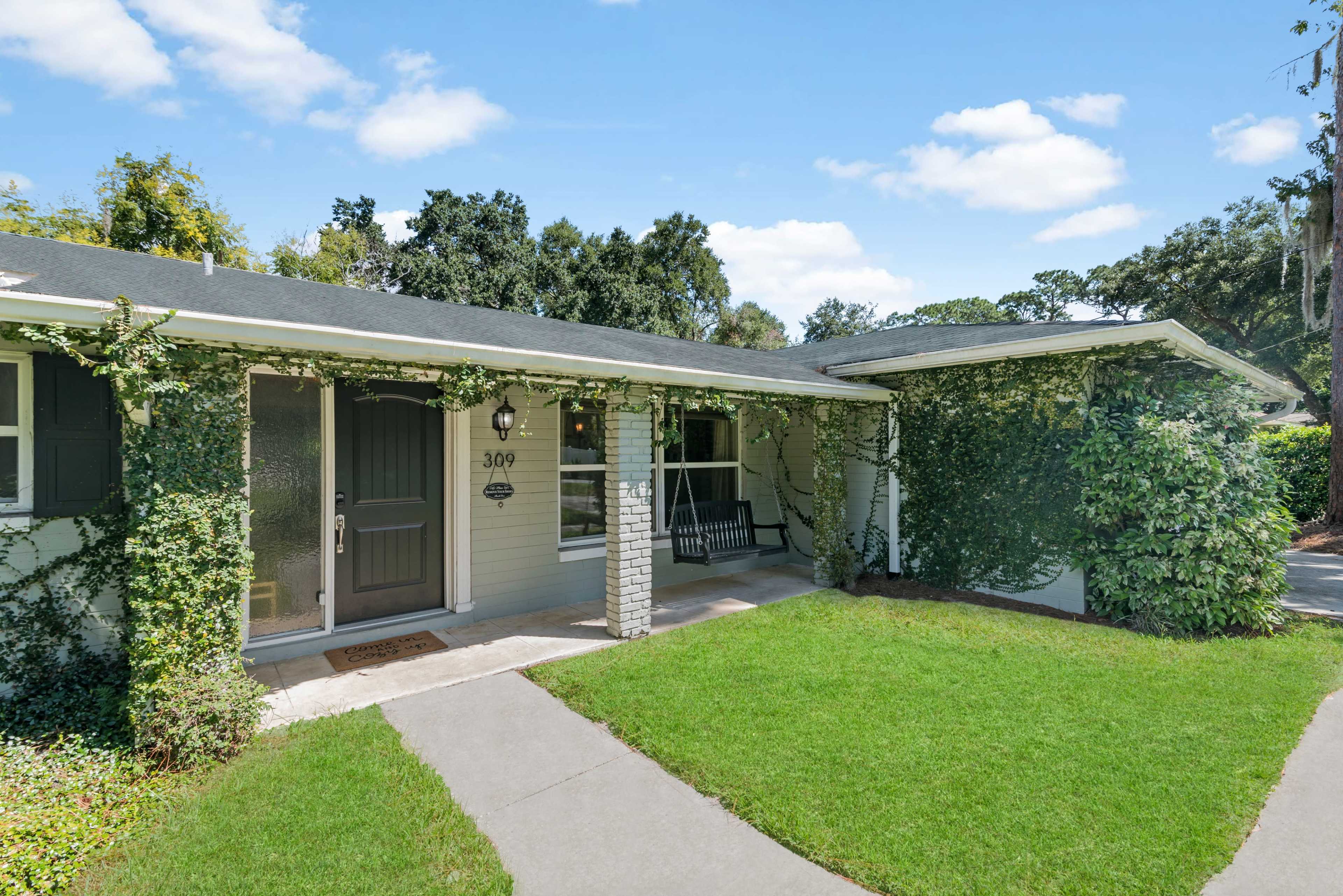 A single-story house with a stone and wood entrance, surrounded by greenery and a well-maintained lawn.