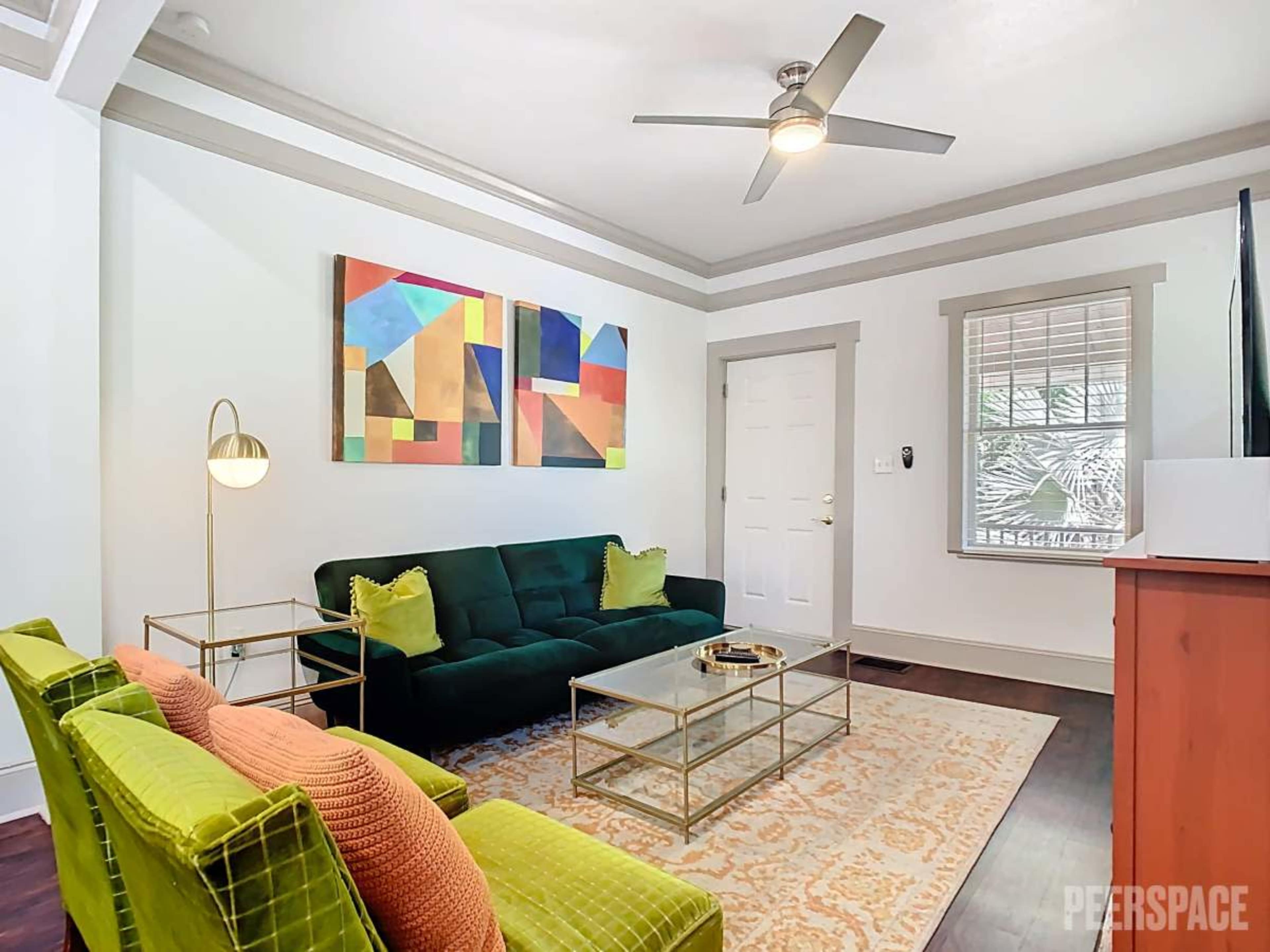 The living room features a green velvet sofa, two matching chairs, a glass coffee table, and a colorful abstract painting on the wall.