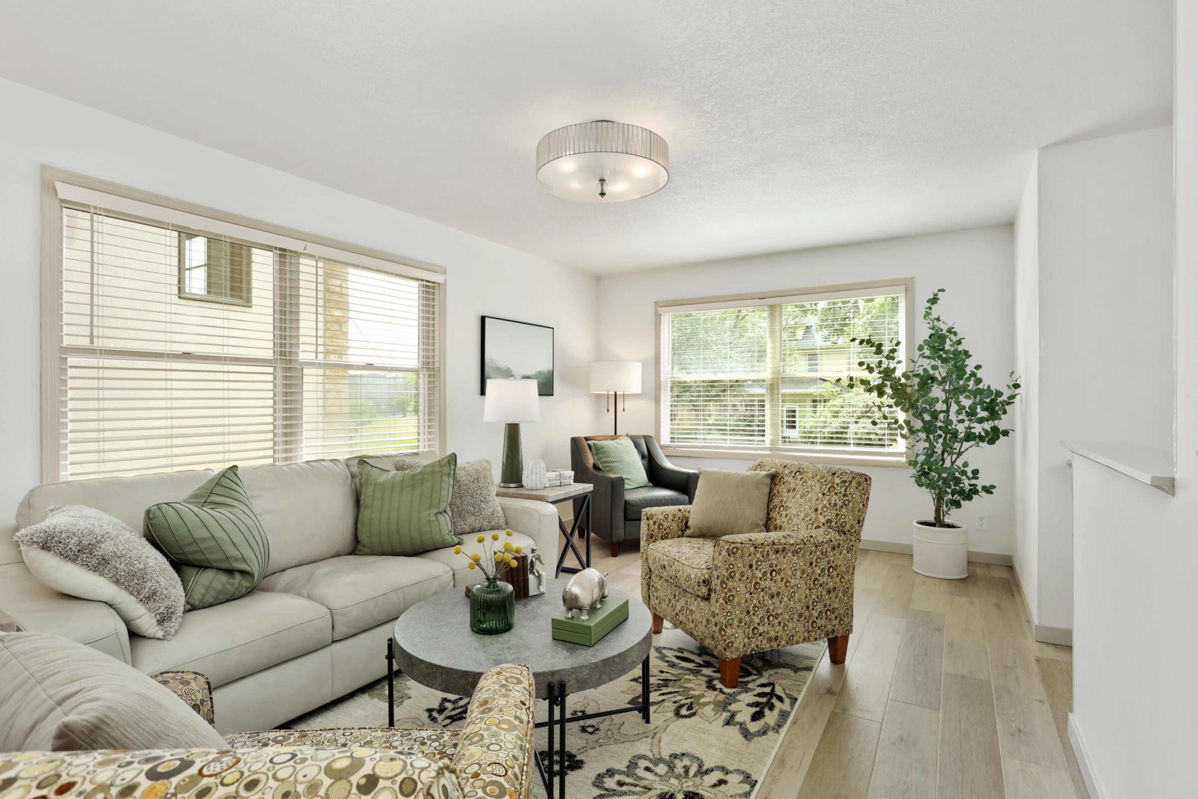 The living room features a light-colored sofa, a patterned armchair, a round coffee table, and large windows allowing natural light to fill the space.