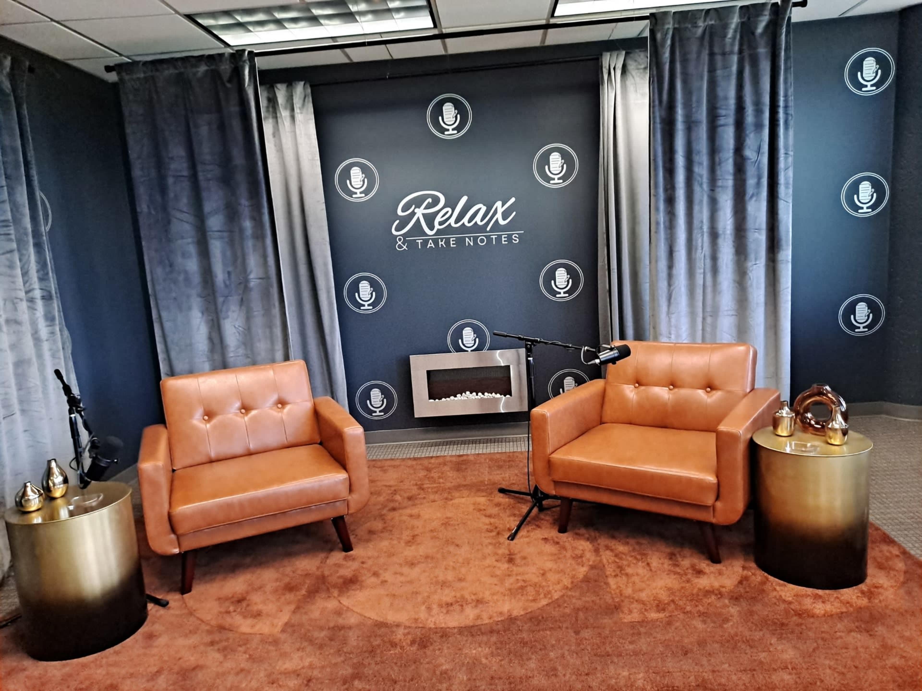 A cozy indoor setting with two brown leather chairs, a small golden side table on each side, a decorative wall featuring microphones, and a modern fireplace.