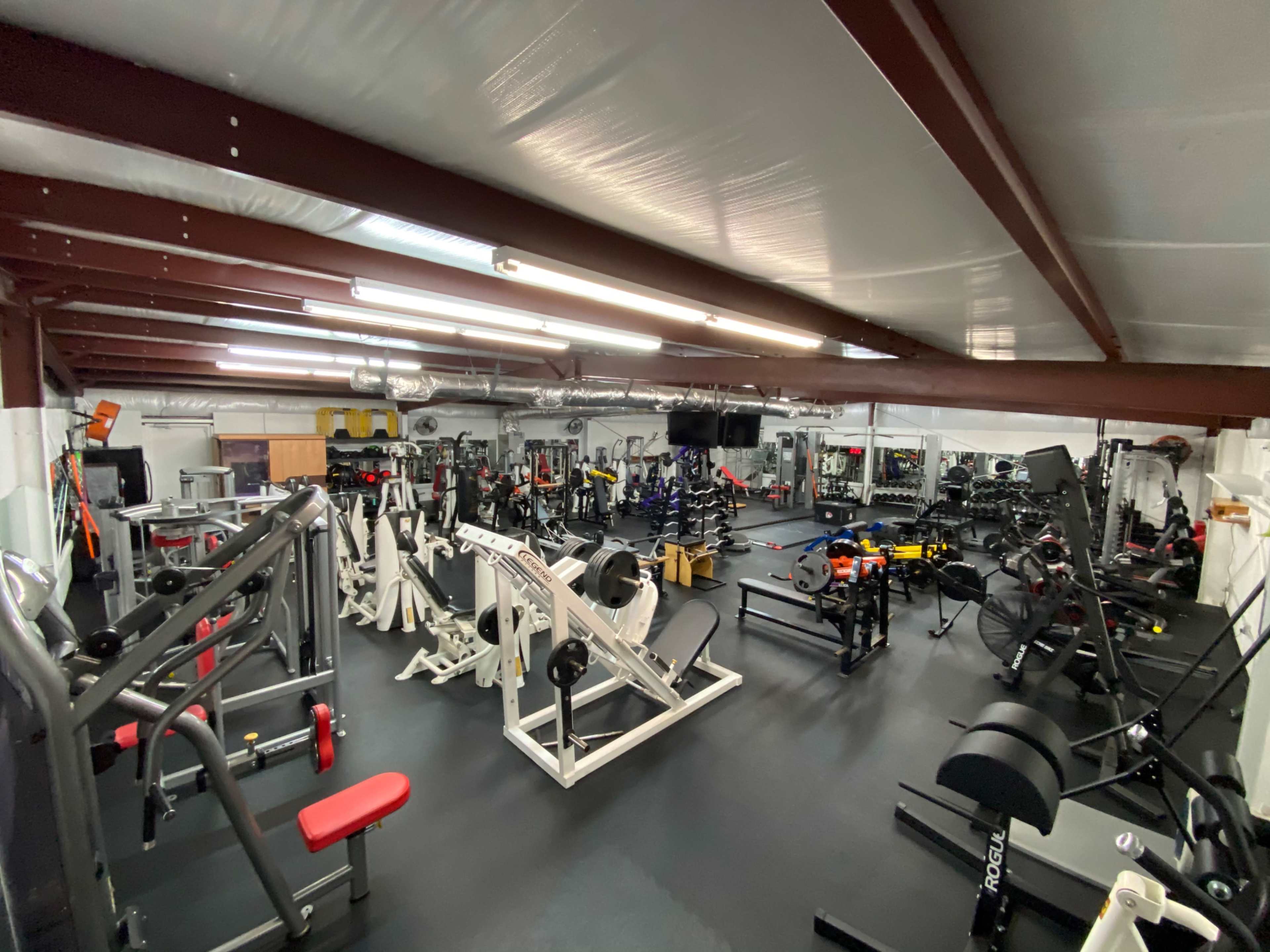 A spacious gym interior filled with various exercise equipment, including weight machines, free weights, and cardio stations.