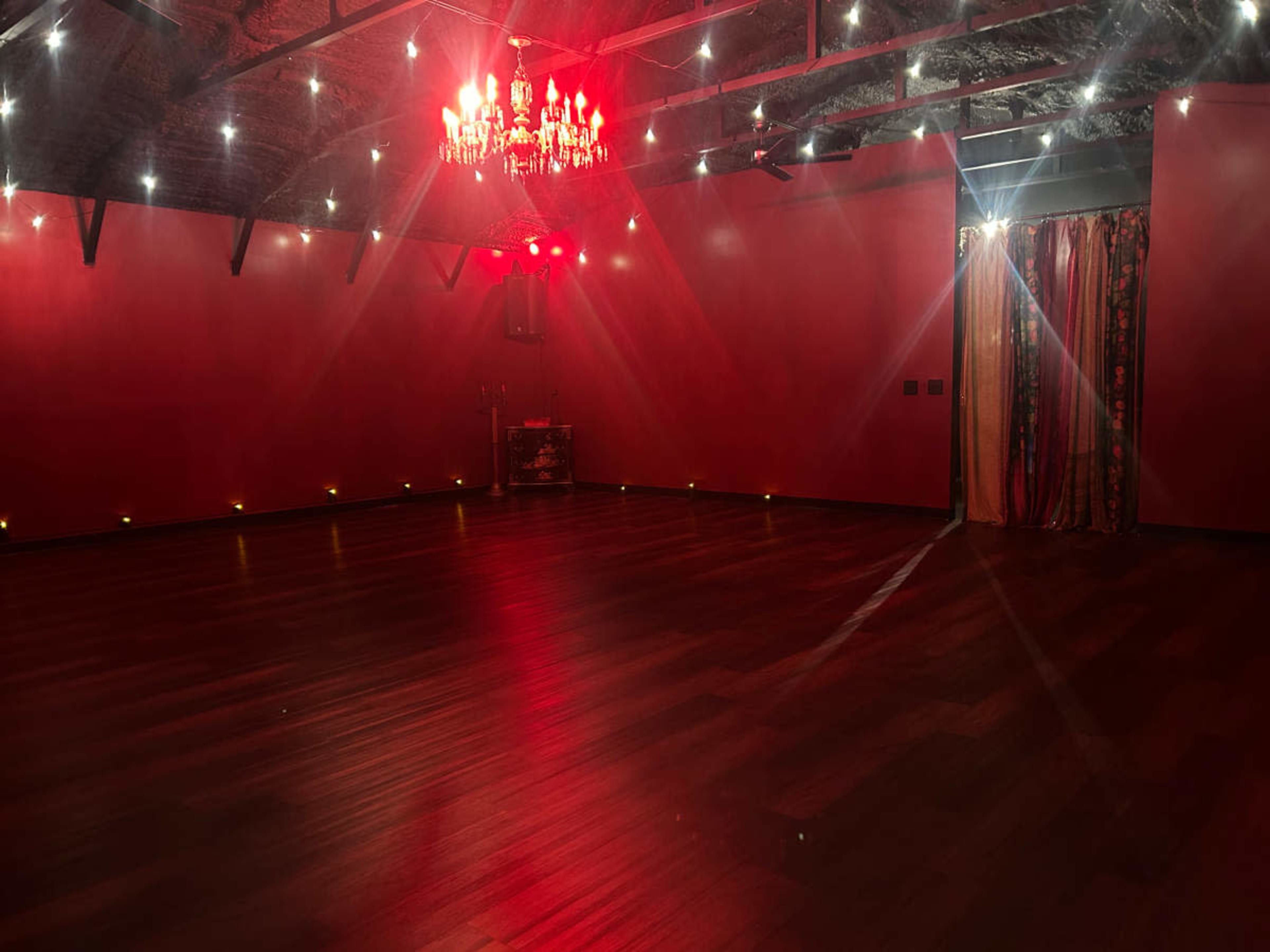 The image shows a spacious room with red walls, a chandelier, and soft lighting illuminating the wooden floor.