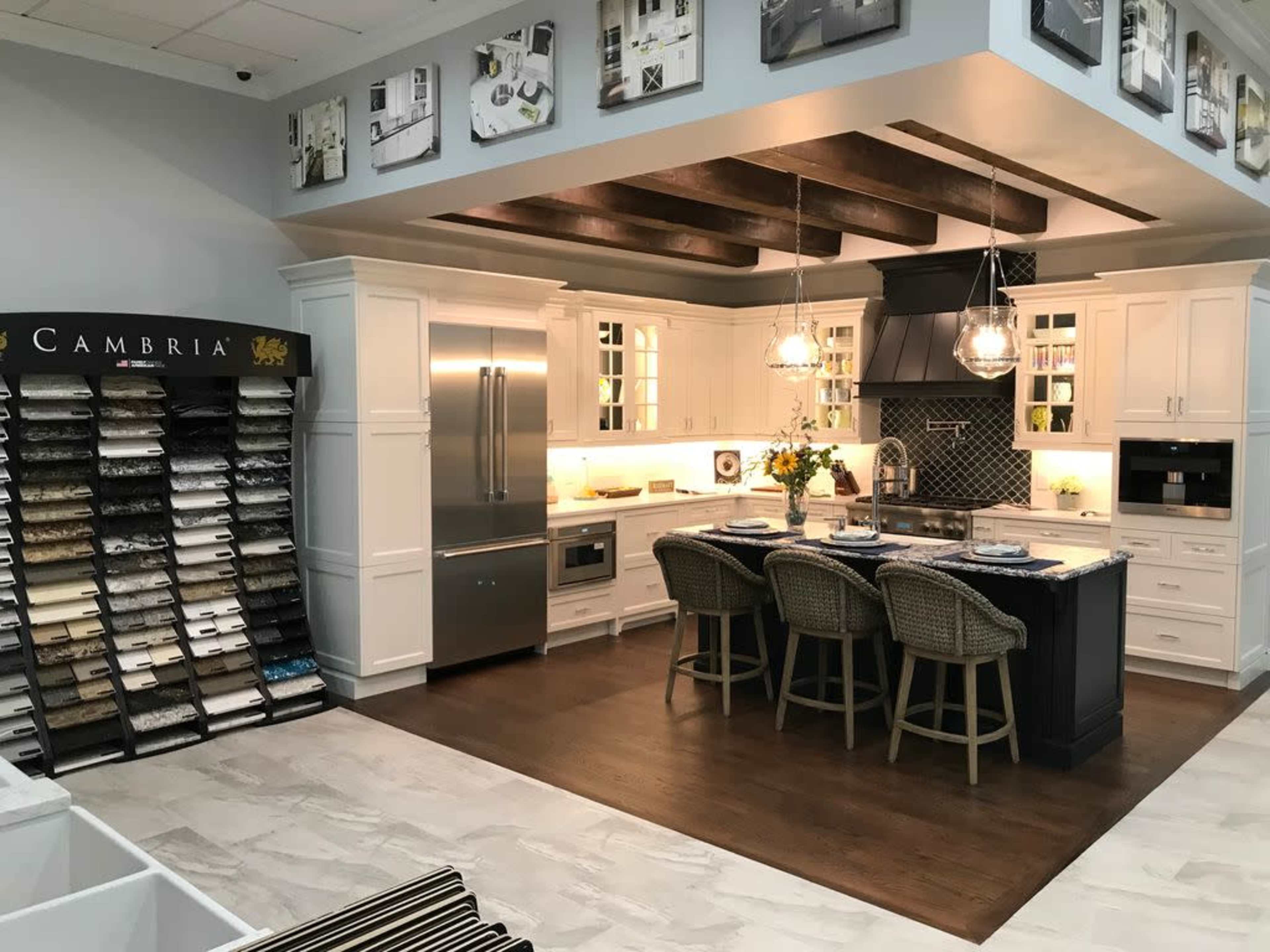 A modern kitchen display with white cabinets, a central island, and a selection of countertop samples on the left.