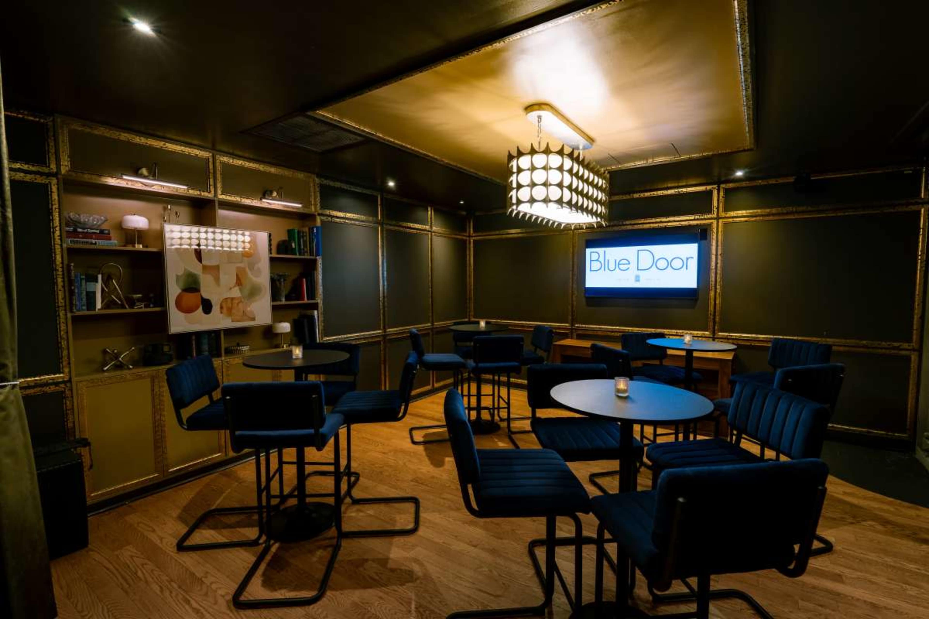The image shows a dimly lit interior of a lounge or bar named "Blue Door," featuring several round tables and high-backed chairs against a backdrop of decorative shelves.