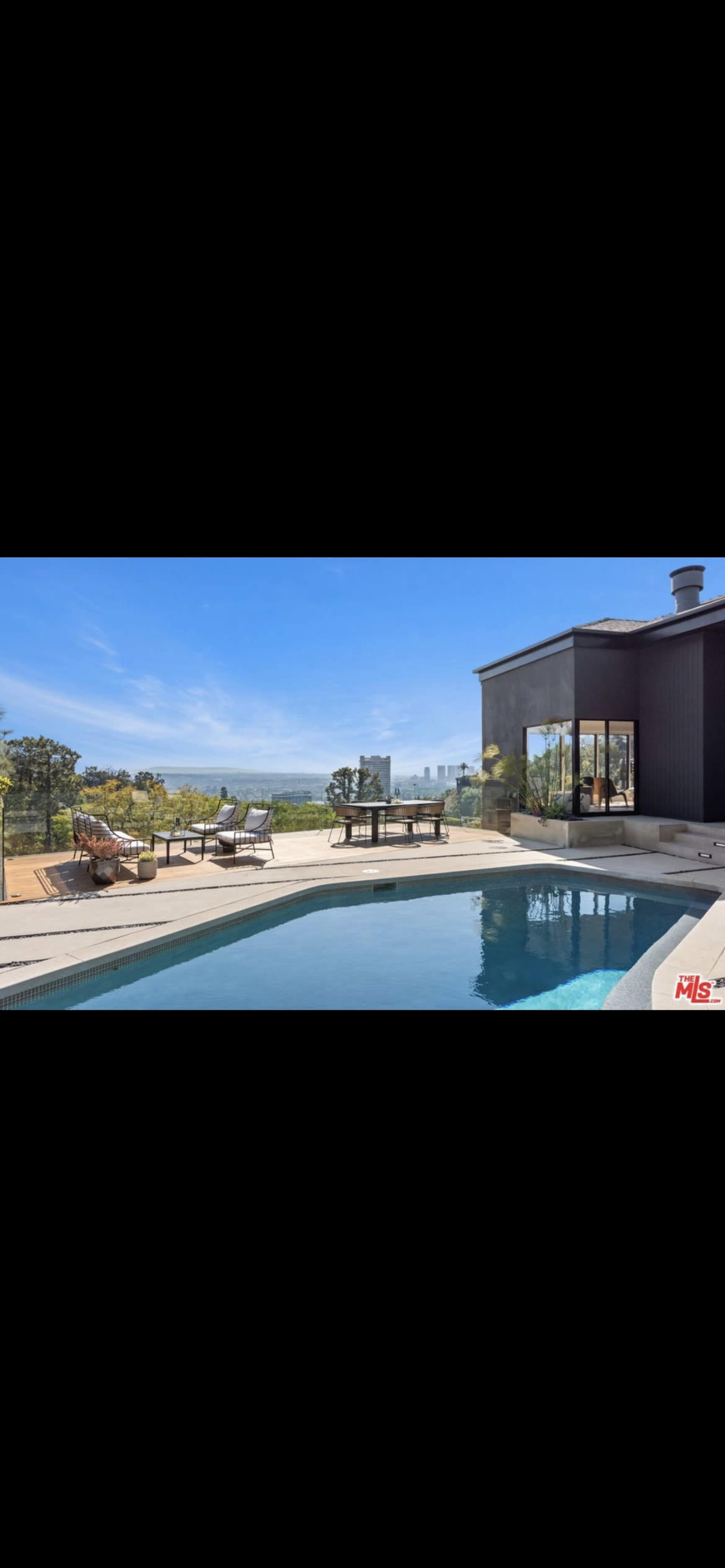 A modern house with a swimming pool and a view of a city skyline in the background.
