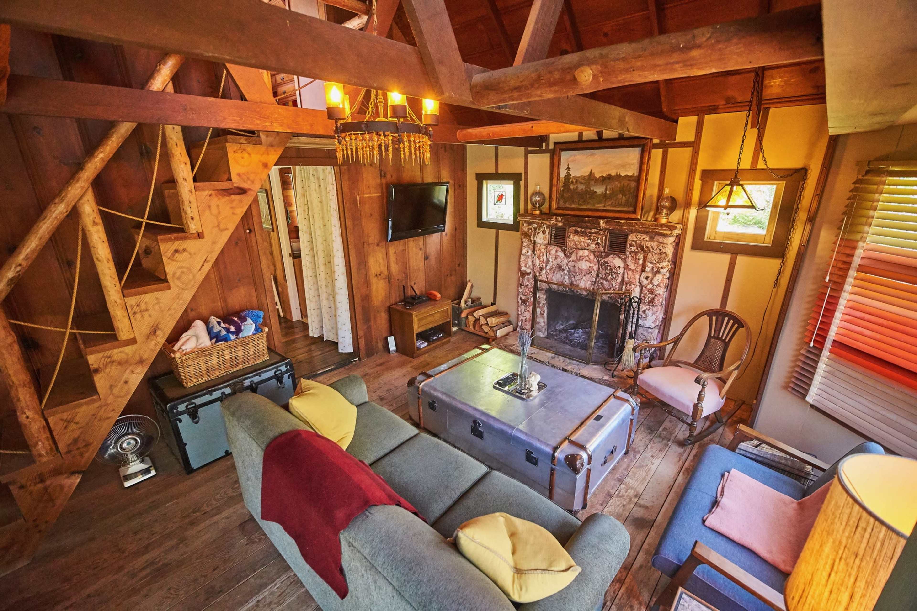 A cozy, rustic living room with wooden beams, a stone fireplace, a television, and a mix of comfortable seating options.