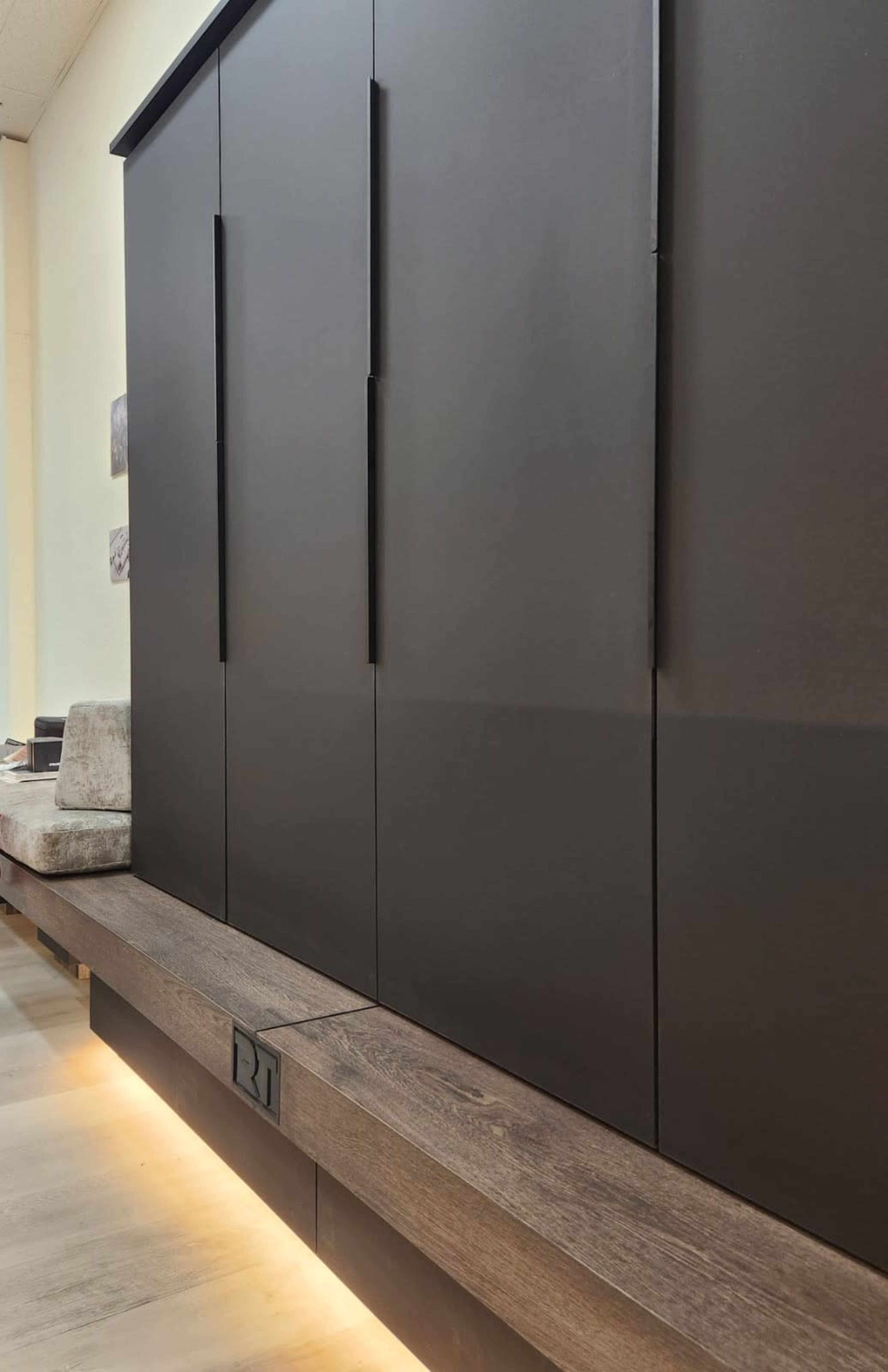 The image shows a modern wall unit with dark cabinet doors and a wooden ledge that features soft underlighting.